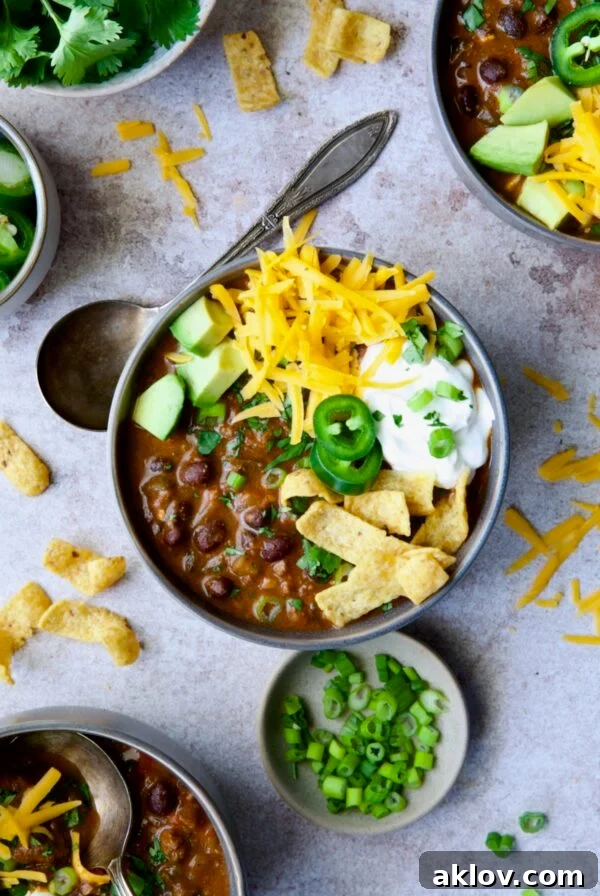 One serving of Beef and Chorizo Chili in gray bowl garnished with avocado, cheddar cheese, sour cream, jalapeno slices and corn chips.