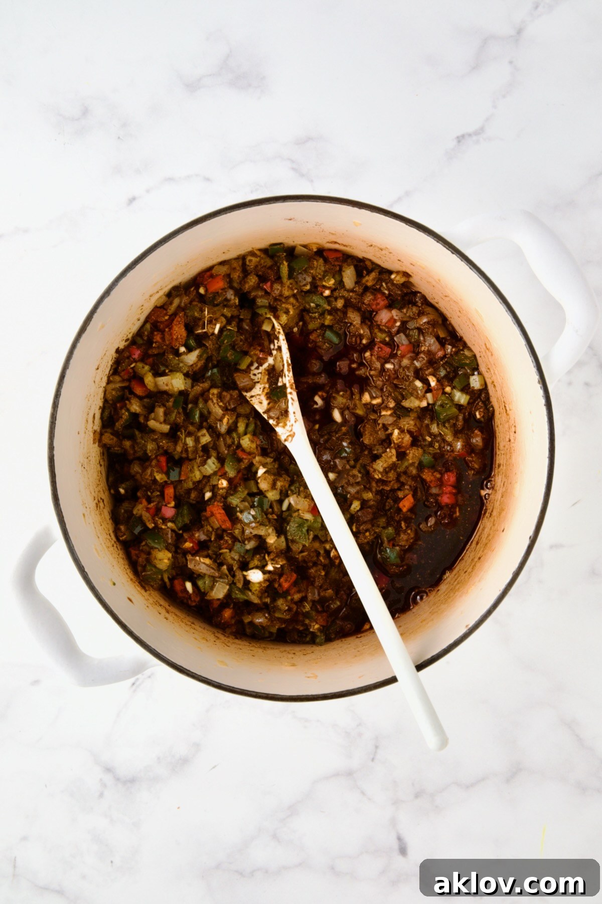 Wine added to spices and vegetables in white enamel Dutch oven.