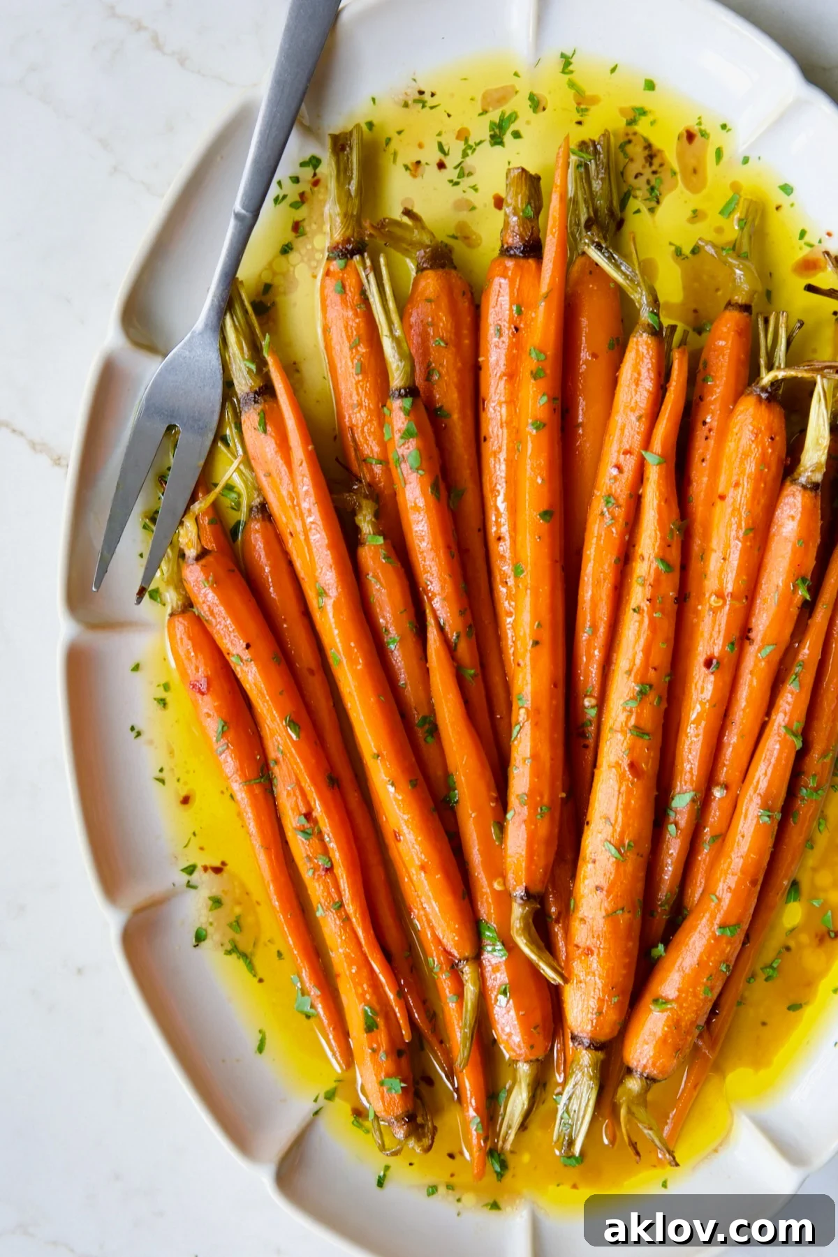 Hot Honey Roasted Carrots on white oval platter with serving fork garnished with fresh parsley.