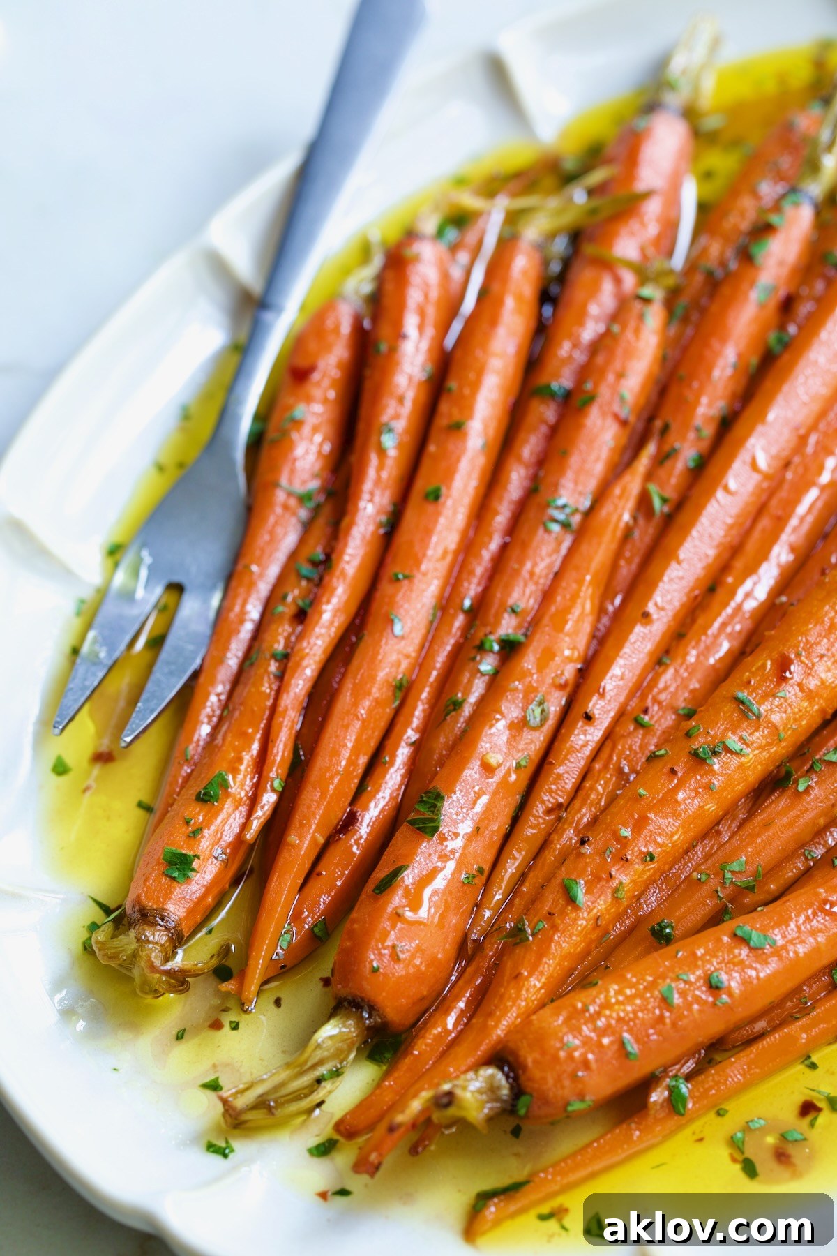 Hot Honey Roasted Carrots on white oval platter with serving fork garnished with fresh parsley.