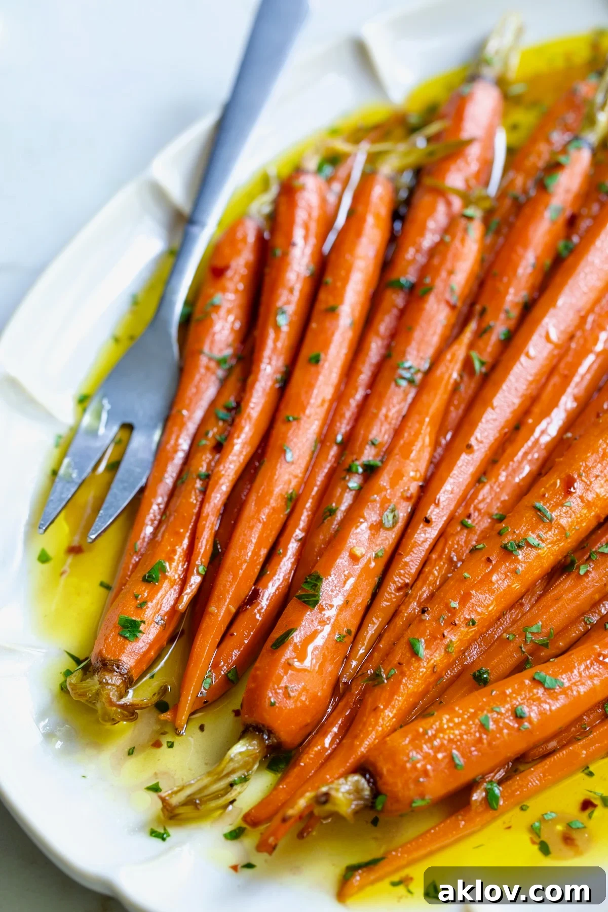 Hot Honey Roasted Carrots on white oval platter with serving fork garnished with fresh parsley.
