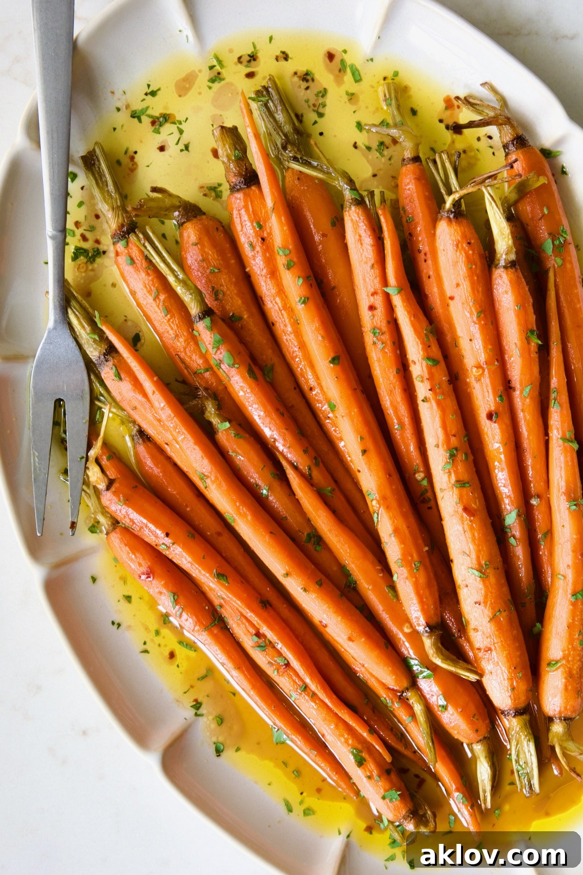 Hot Honey Roasted Carrots on white oval platter with serving fork garnished with fresh parsley.