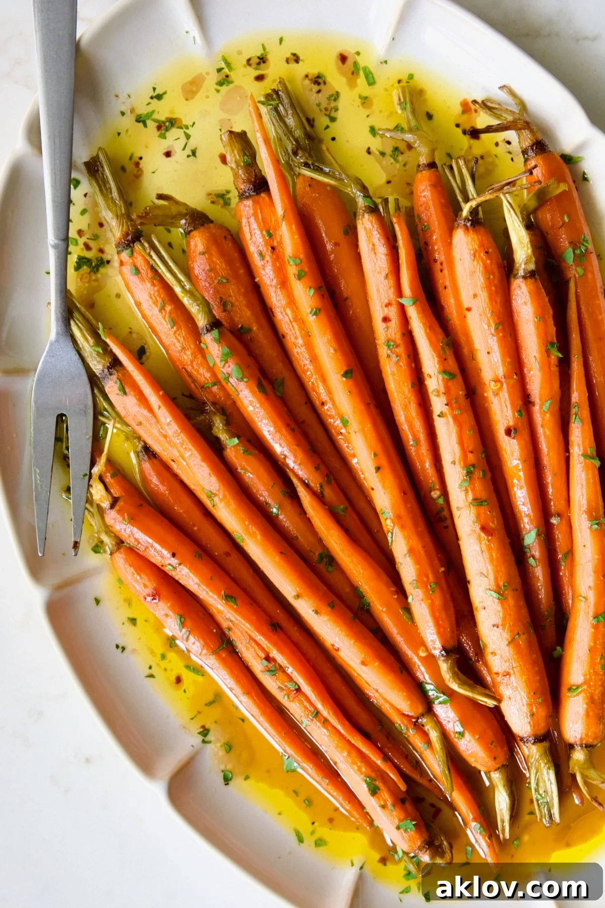 Hot Honey Roasted Carrots on white oval platter with serving fork garnished with fresh parsley.
