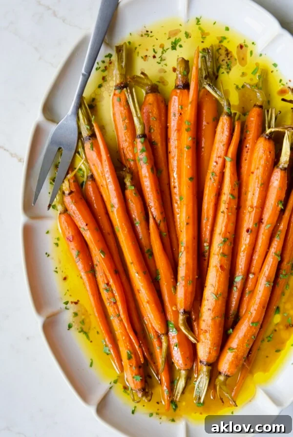 Hot Honey Roasted Carrots on white oval platter with serving fork garnished with fresh parsley.