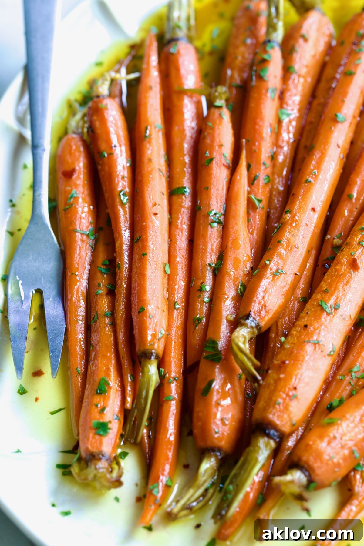 Hot Honey Roasted Carrots on white oval platter with serving fork garnished with fresh parsley.