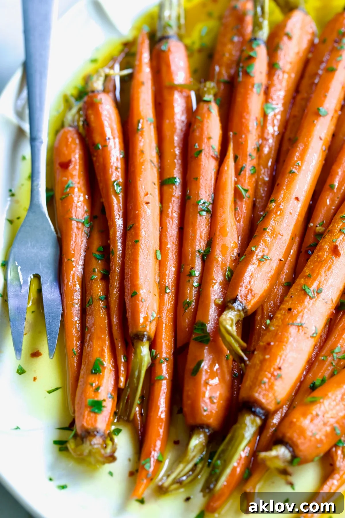 Hot Honey Roasted Carrots on white oval platter with serving fork garnished with fresh parsley.