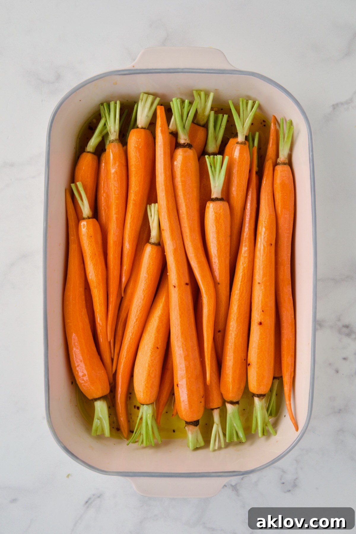 Uncooked carrots added to white rectangle baking dish.