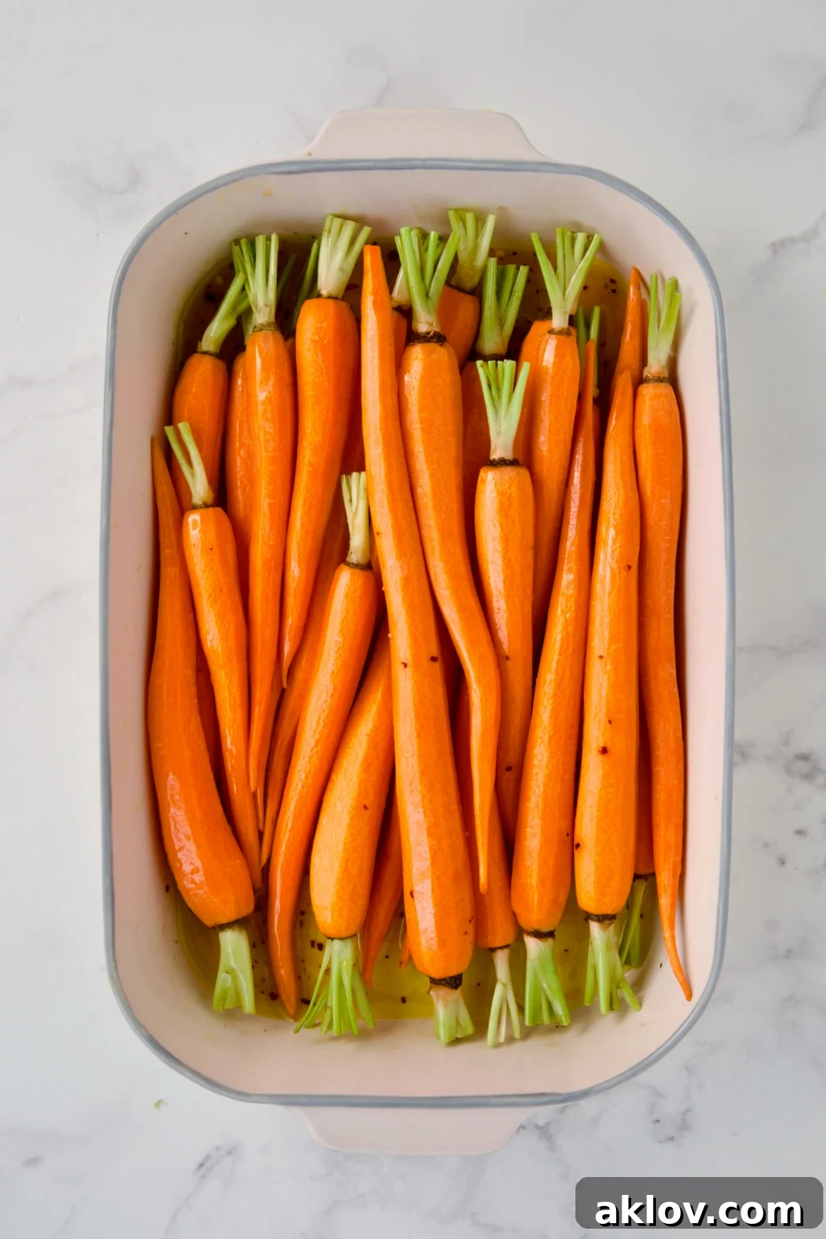 Uncooked carrots added to white rectangle baking dish.