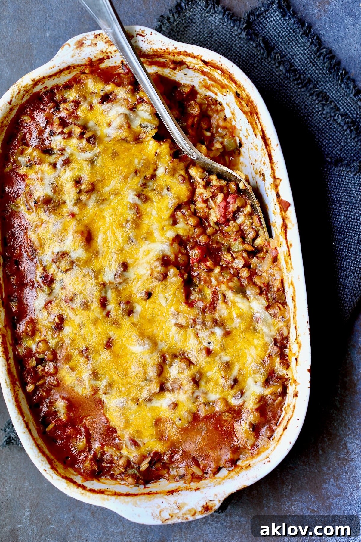 A golden-brown Southwestern Lentil and Brown Rice Bake in an oval white baking dish, with a serving neatly removed, showcasing the cheesy, hearty layers.