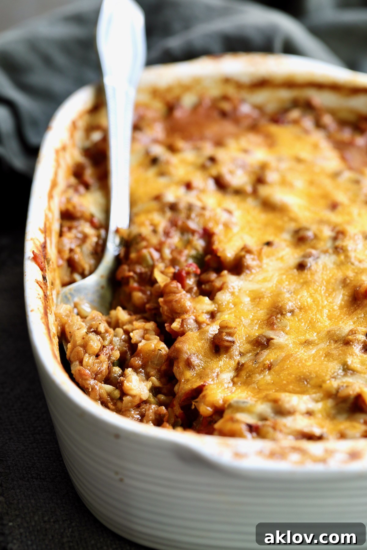 A close-up view of the Southwestern Lentil and Brown Rice Bake in an oval white baking dish, showing its rich texture and cheesy top, with a portion already served.