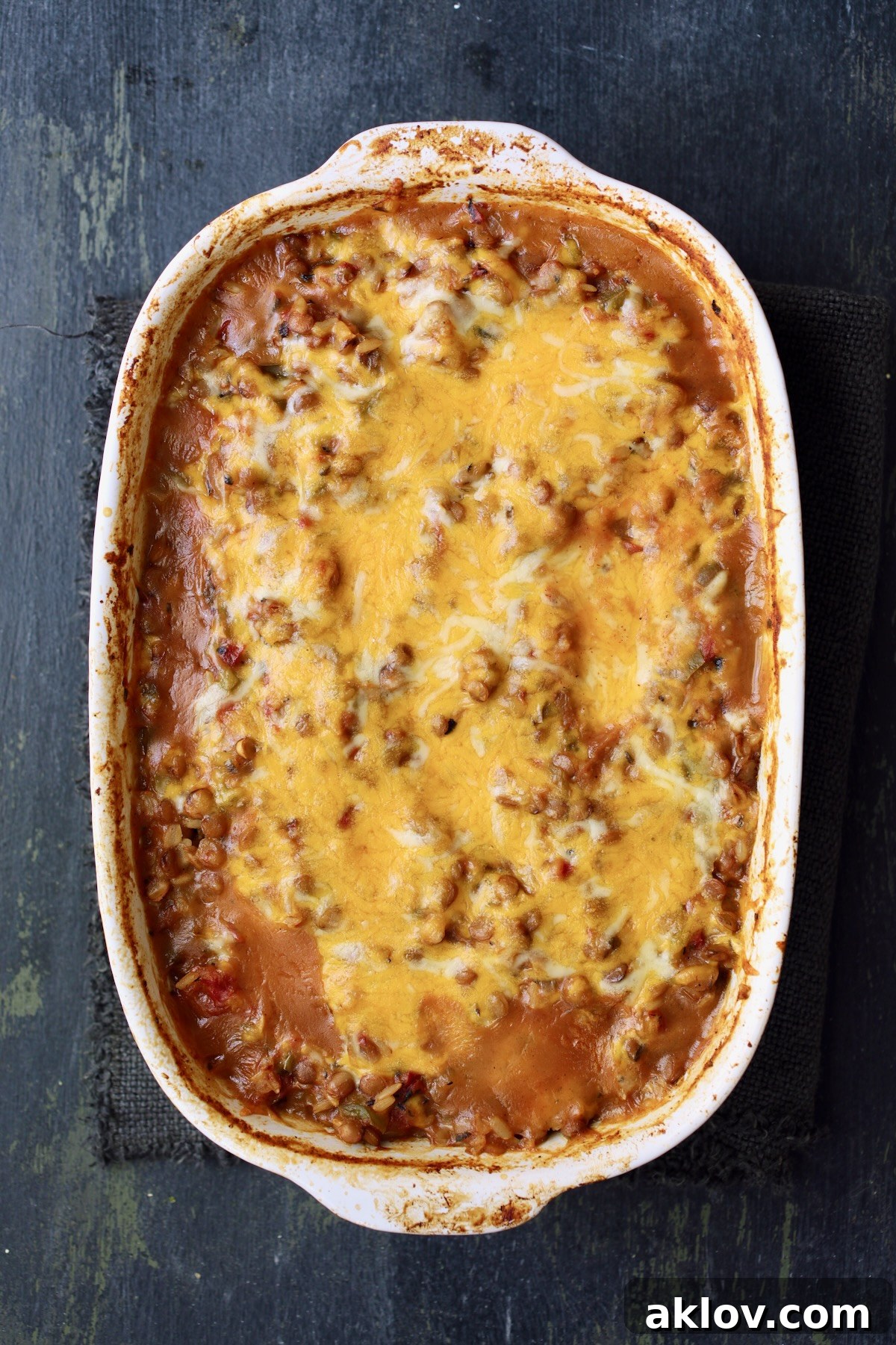 The fully baked Southwestern Lentil and Brown Rice Bake in an oval white baking dish, featuring a rich, bubbly, melted cheese topping, fresh from the oven.