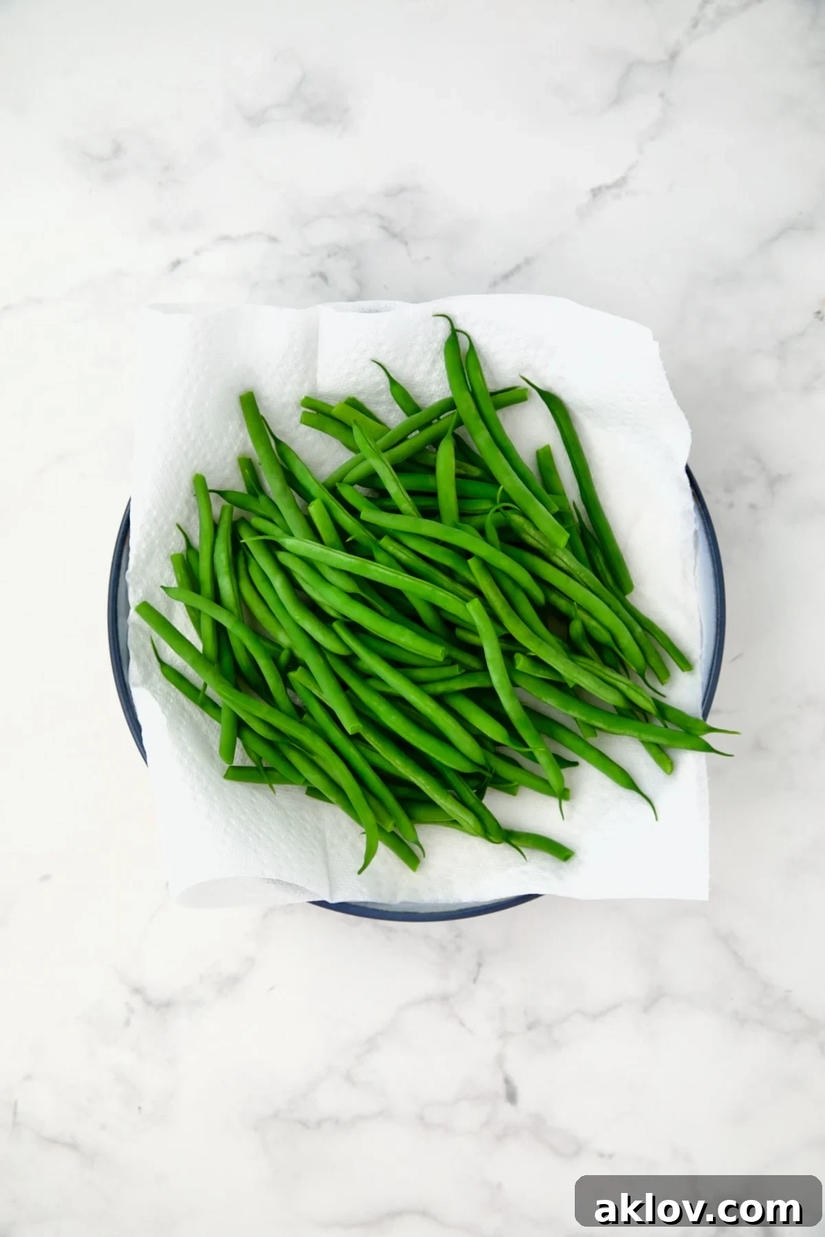 Blanched green beans on paper towel on blue plate.