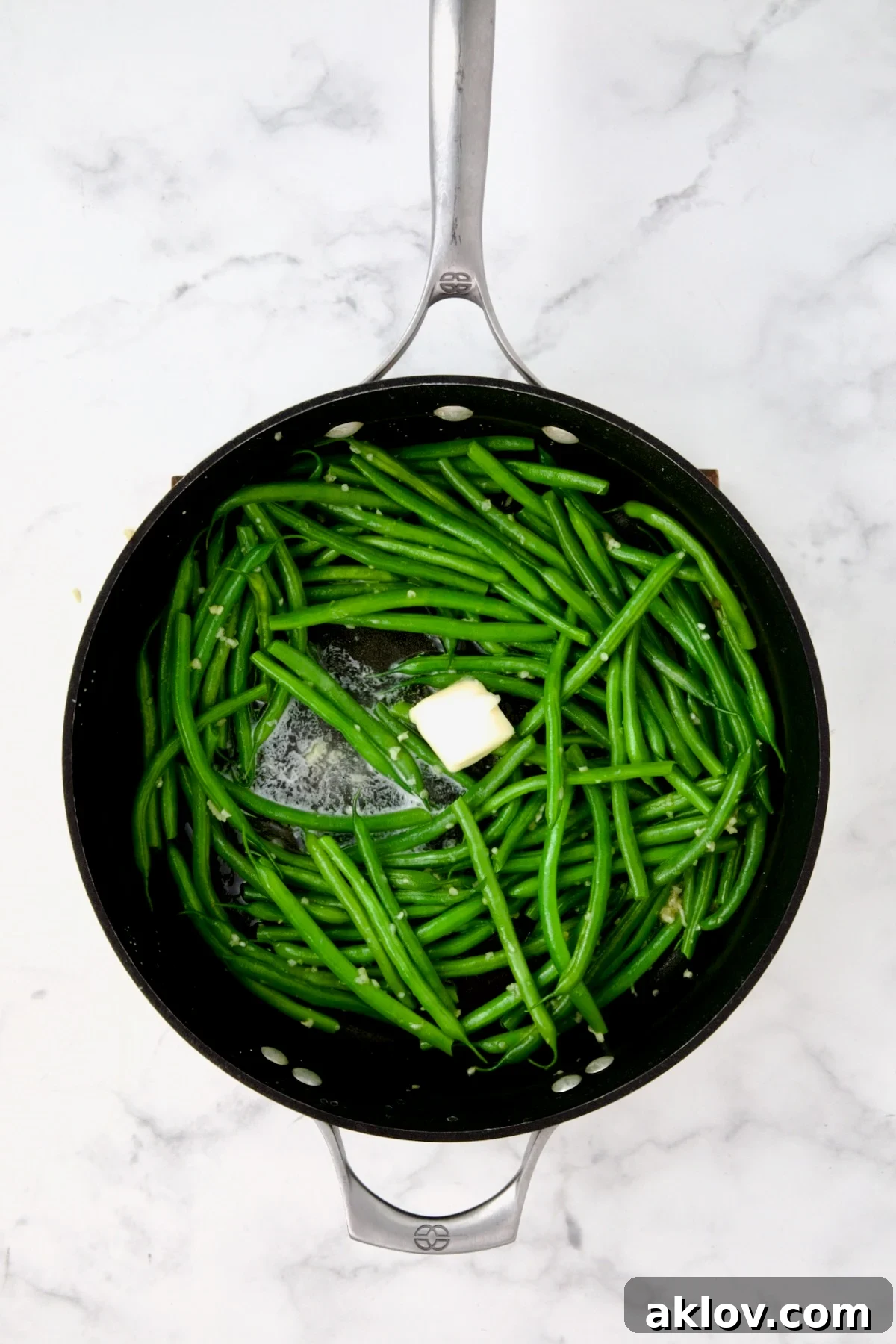 Butter being melted over green beans in nonstick skillet.