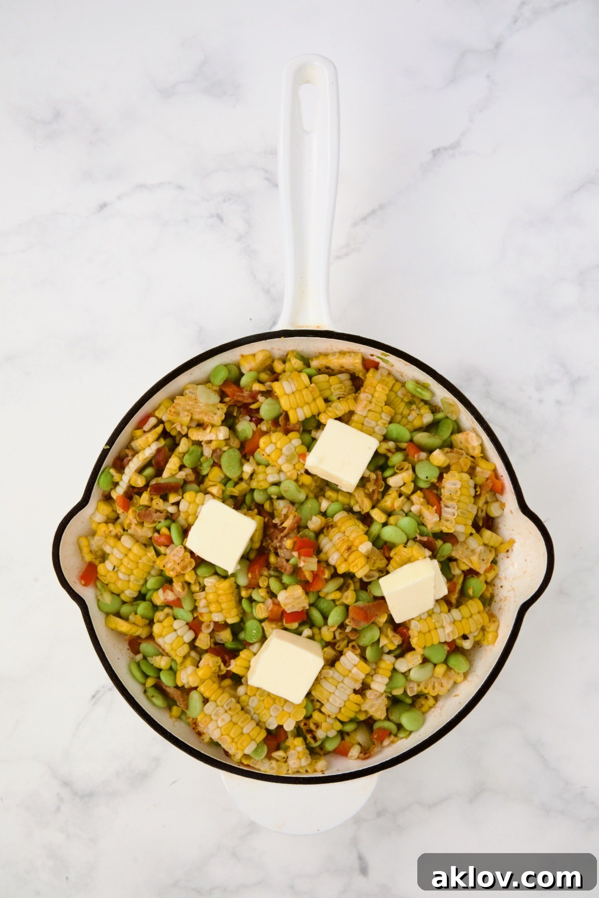 Succotash in white enamel cast iron skillet with four pats of butter on top.