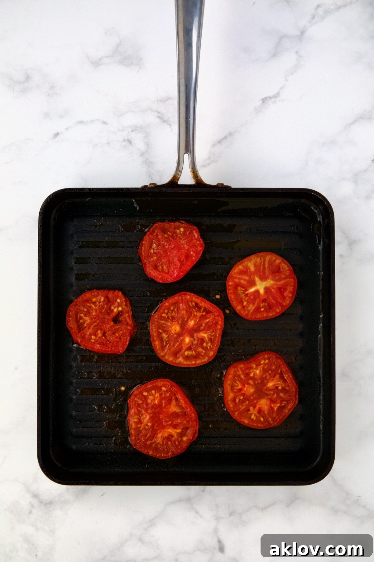 Six tomato slices being grilled on grill pan.