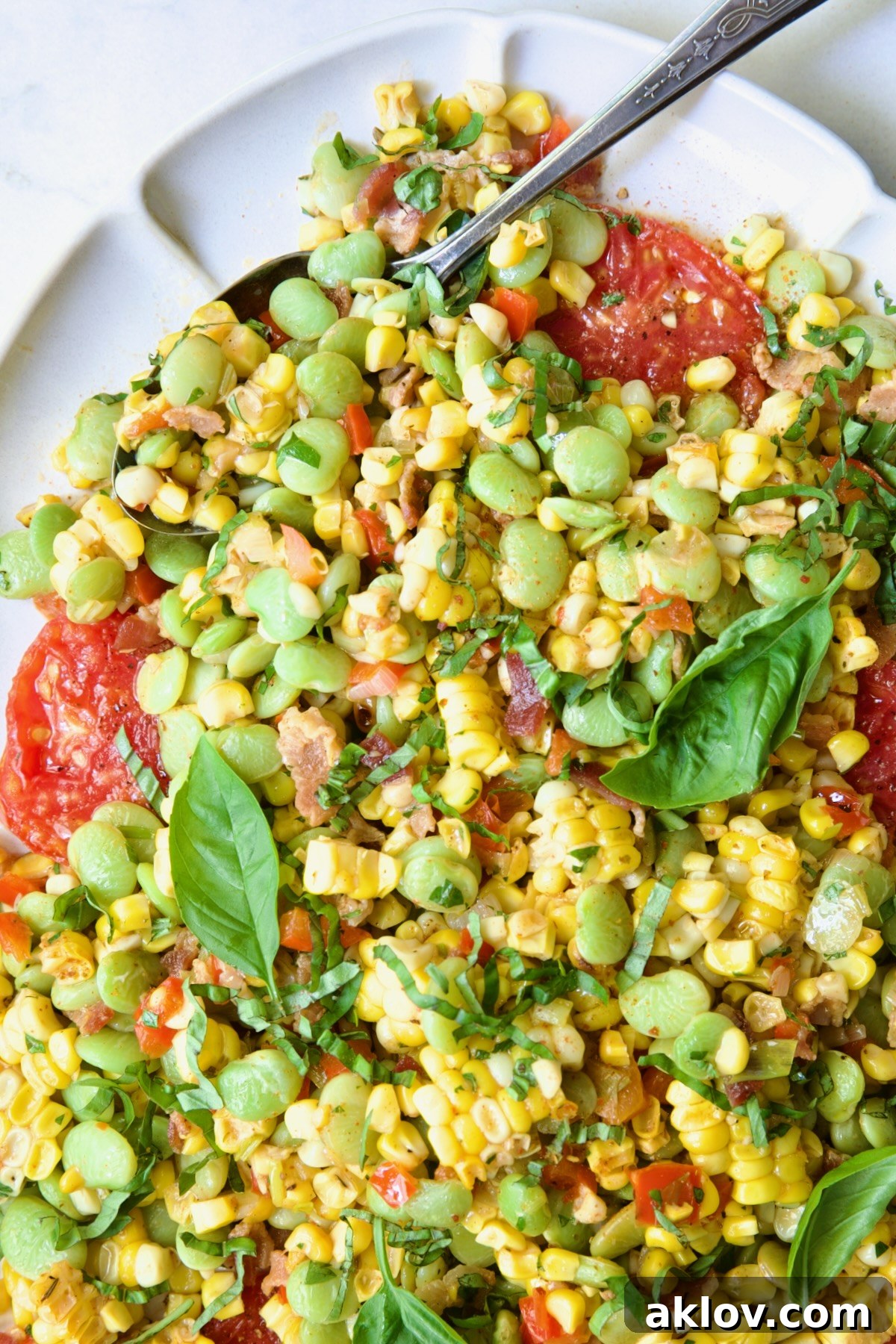 Grilled Corn Succotash on white oval platter with serving spoon garnished with fresh basil leaves.