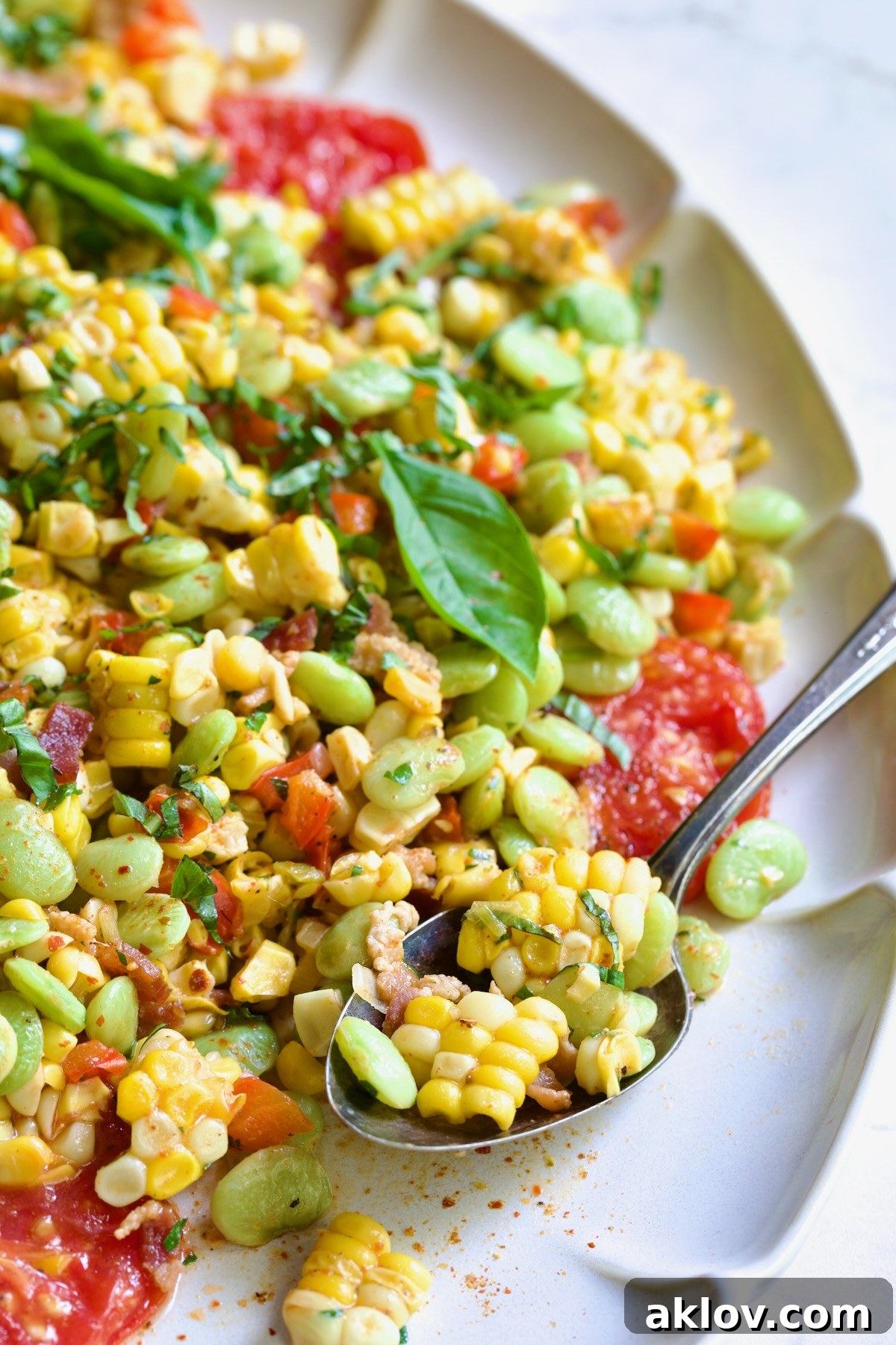 Grilled Corn Succotash garnished with fresh basil on white oval platter with serving spoon scooping some up.