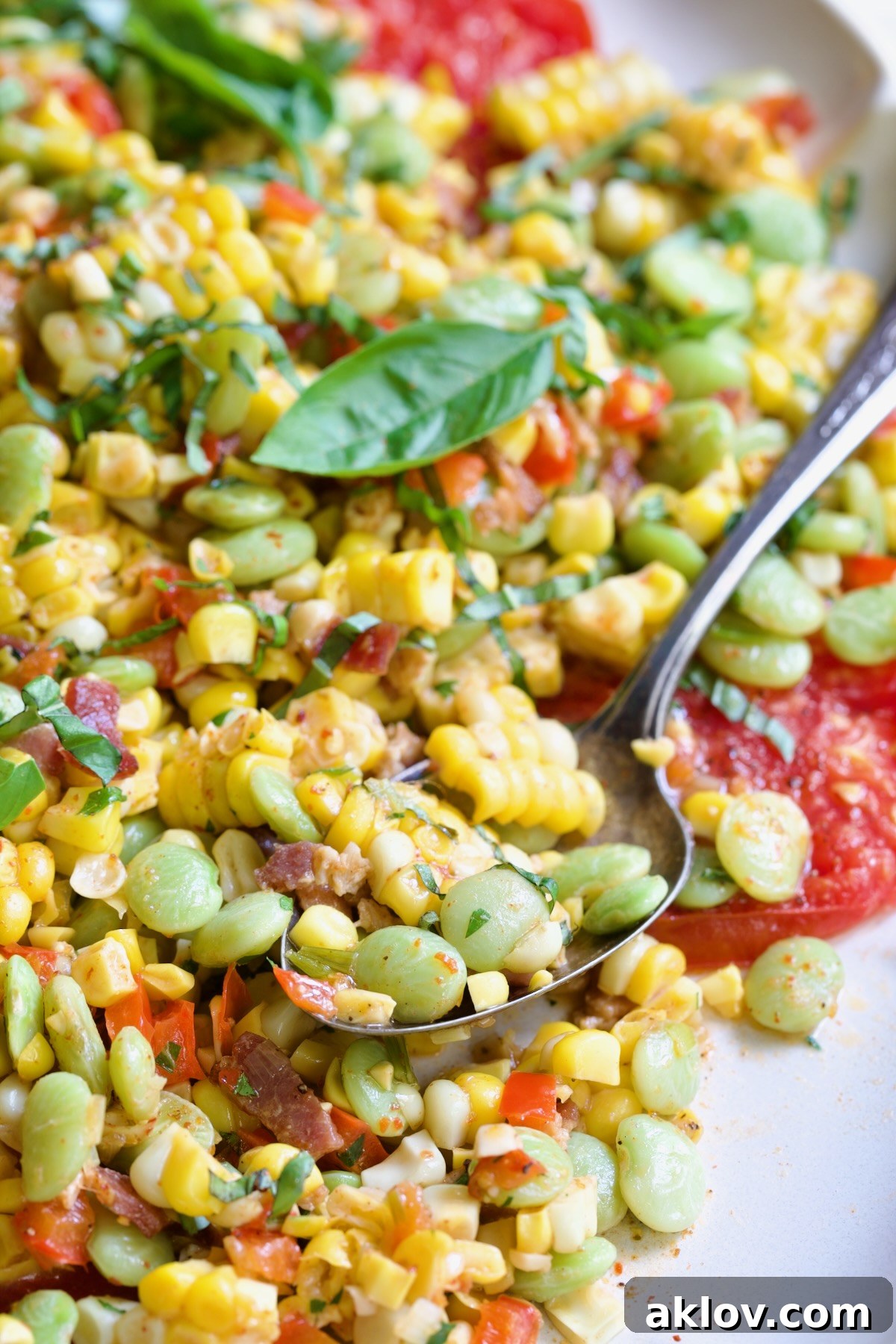 Grilled Corn Succotash garnished with fresh basil on white oval platter with serving spoon scooping some up.