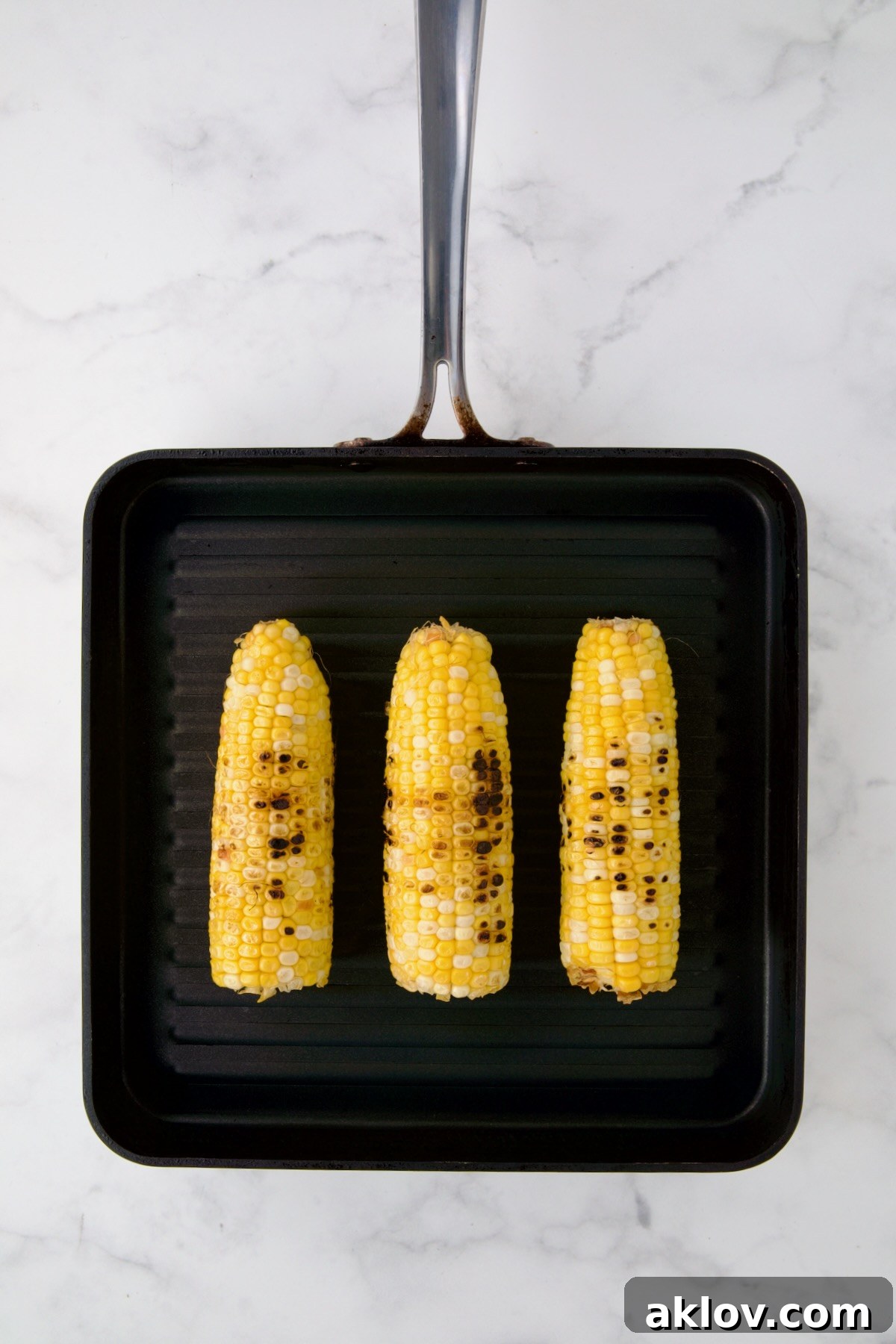 Three ears of corn being grilled on grill pan.
