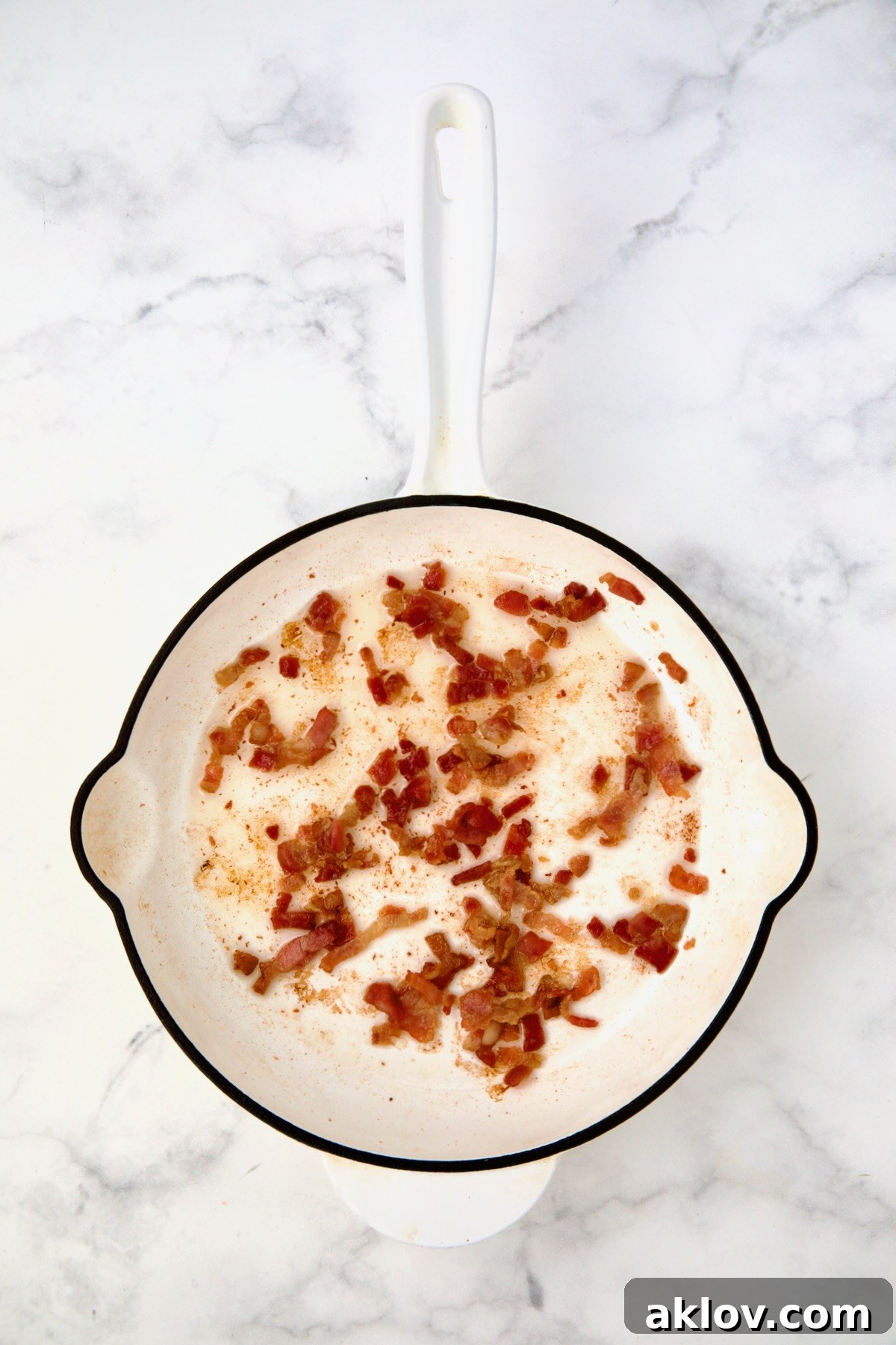 Bacon being crisped in white enamel cast iron skillet.