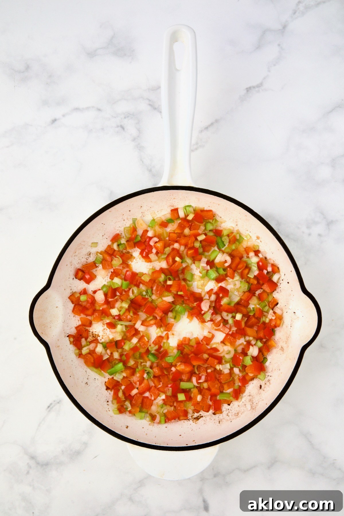 Cooked red bell pepper and scallion in white enamel cast iron skillet.