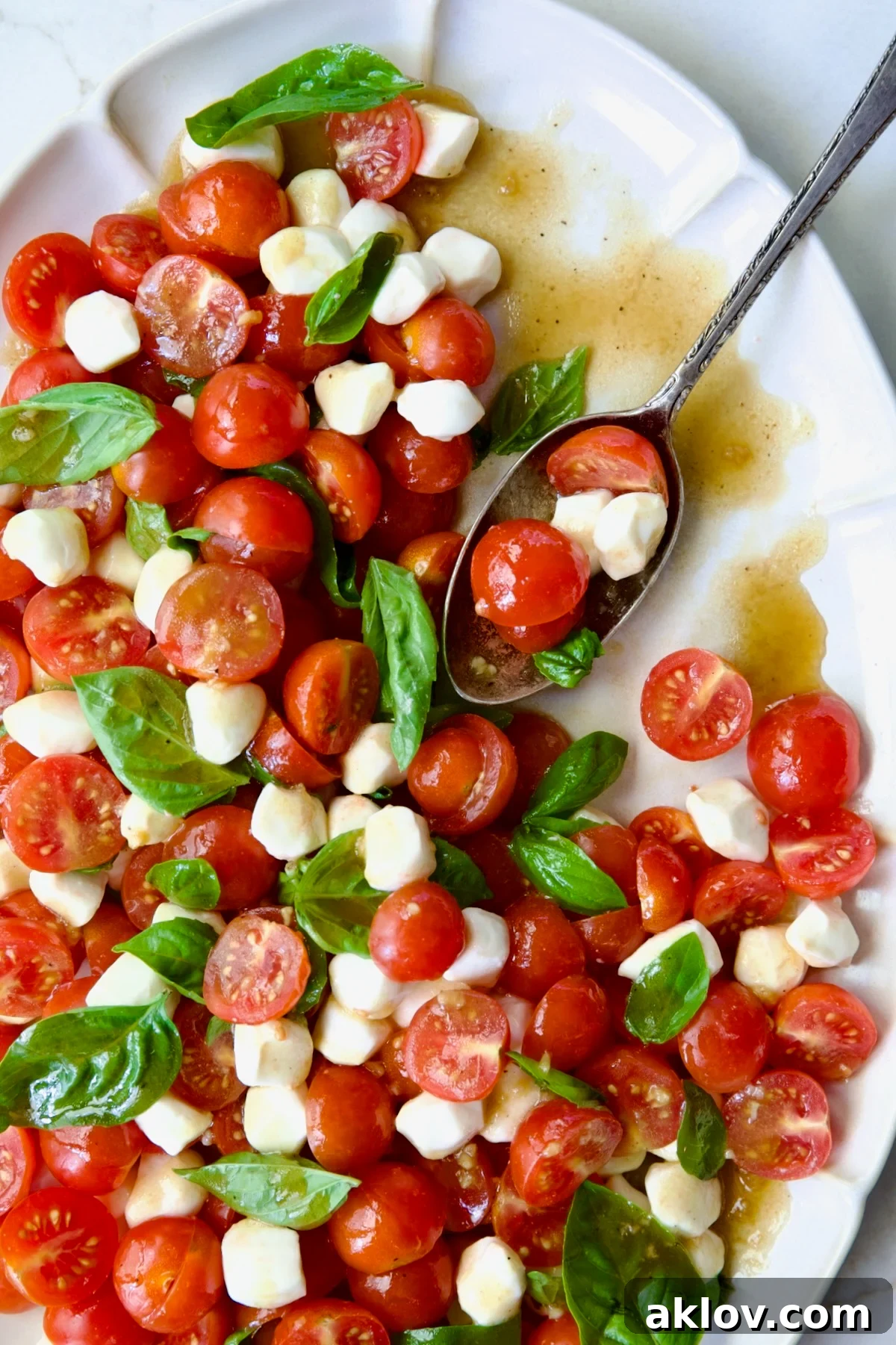Vibrant Caprese Salad with Cherry Tomatoes, mozzarella pearls, and fresh basil, artfully arranged on a white oval platter, ready to be served.