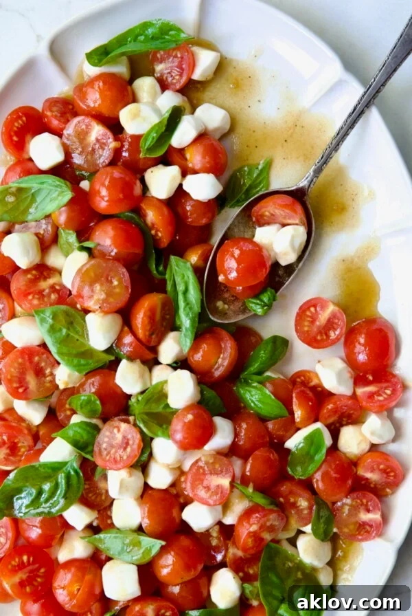 Caprese Salad with Cherry Tomatoes on a white oval platter with a serving spoon.