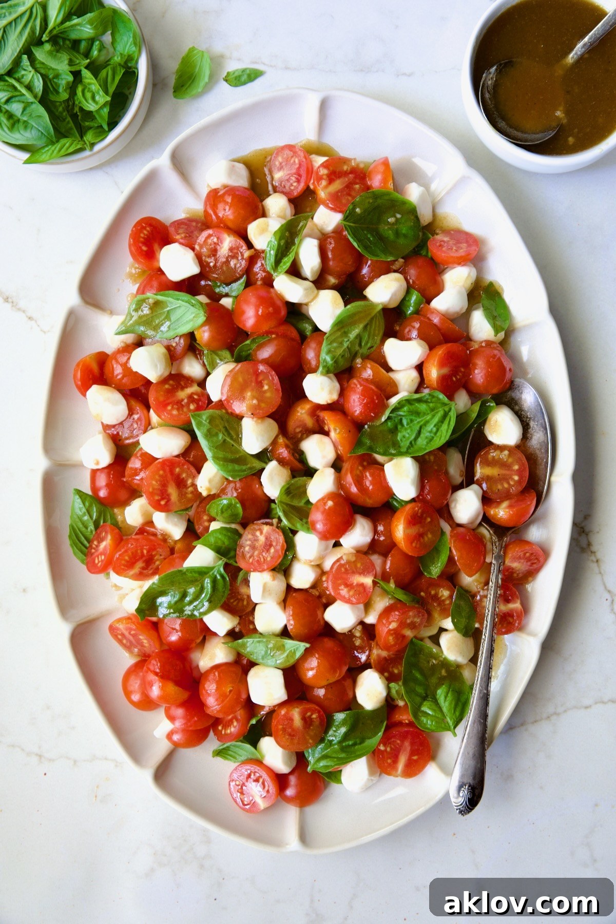 The finished Caprese Salad with Cherry Tomatoes, dressed and presented on a white oval platter with a serving spoon.