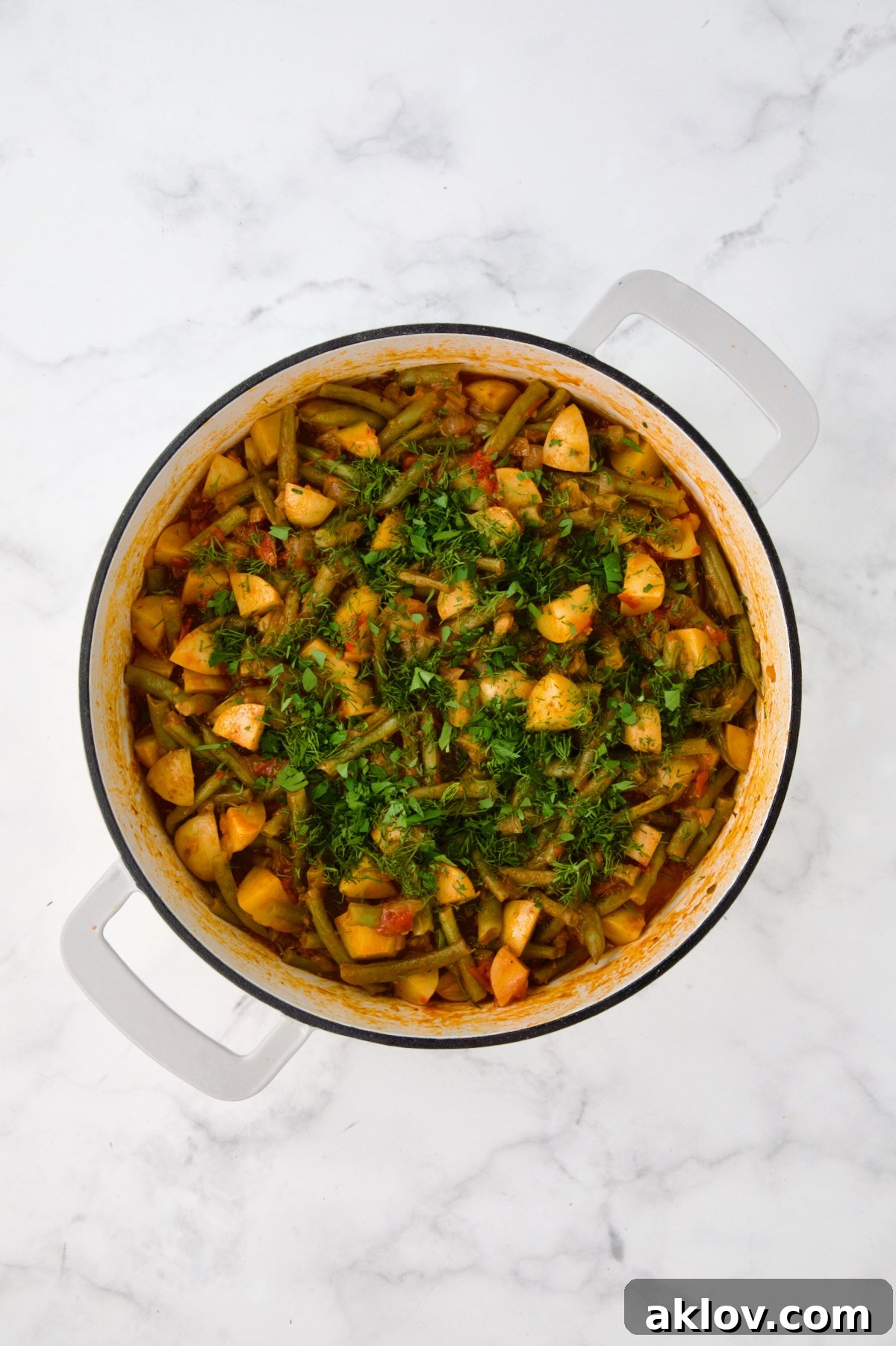 Cooked Fasolakia in white enamel cast iron skillet after herbs added.