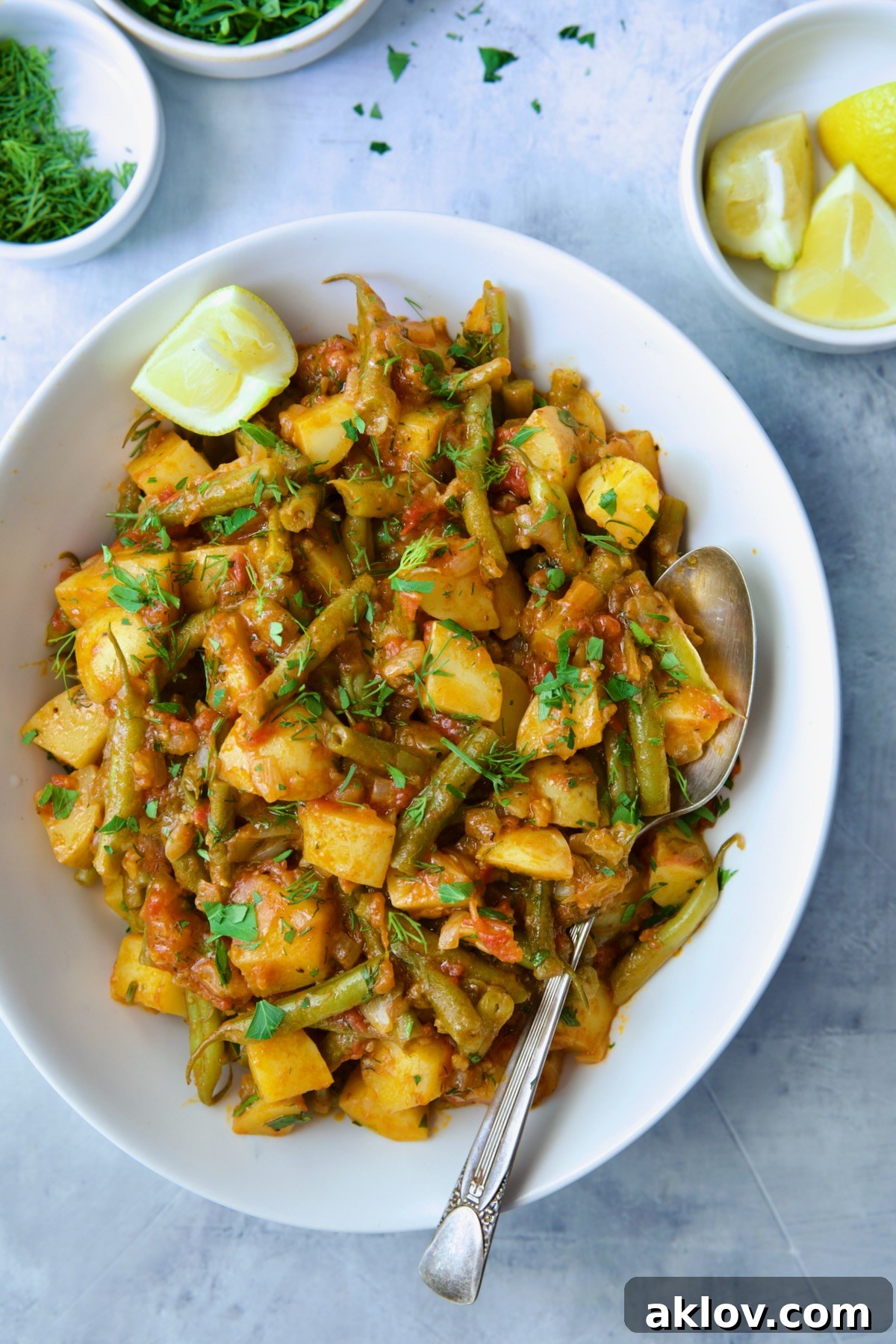 Fasolakia in oval white serving bowl garnished with fresh herbs and lemon wedges.