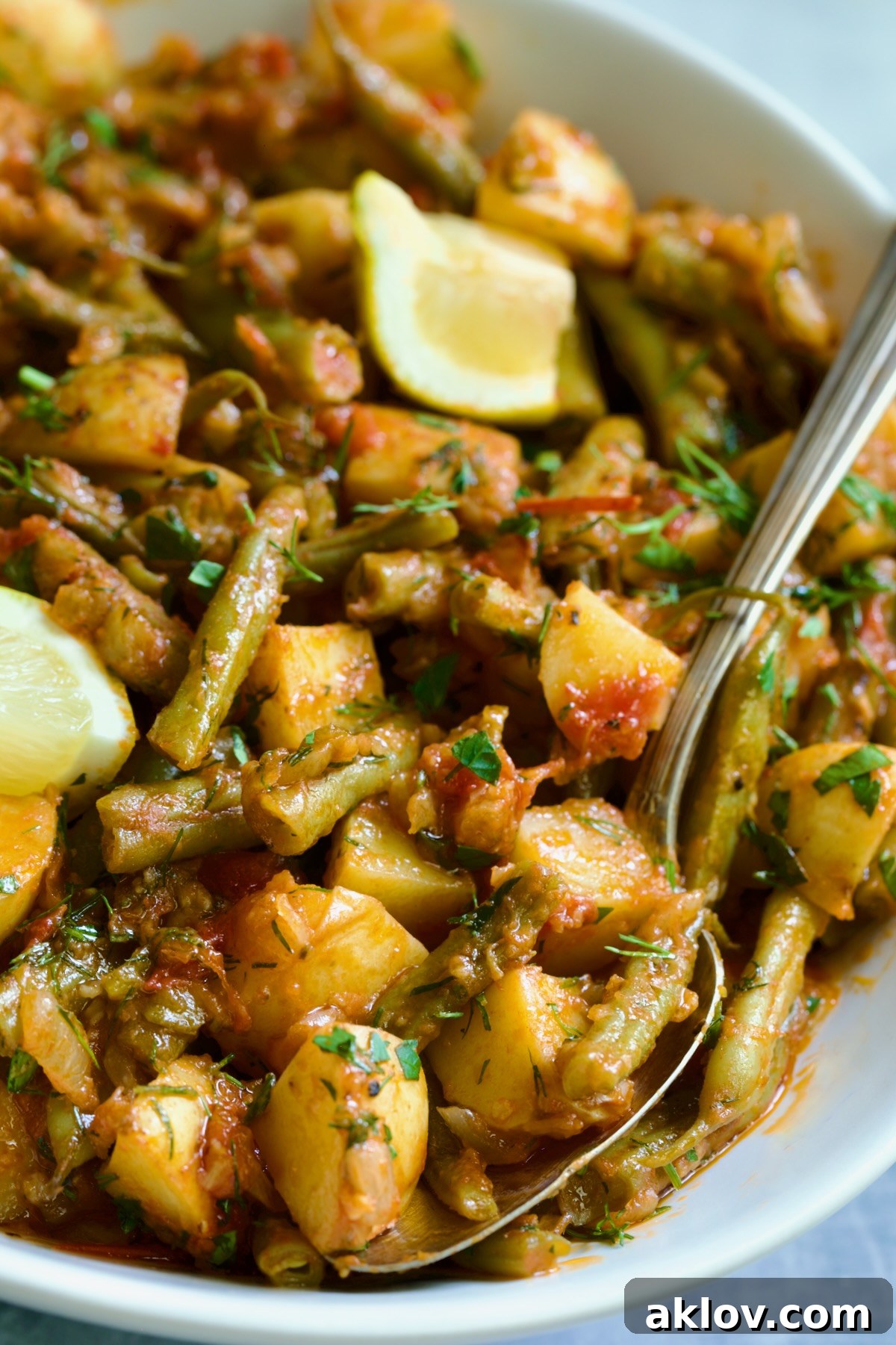 Fasolakia in oval white serving bowl garnished with fresh herbs and lemon wedges.