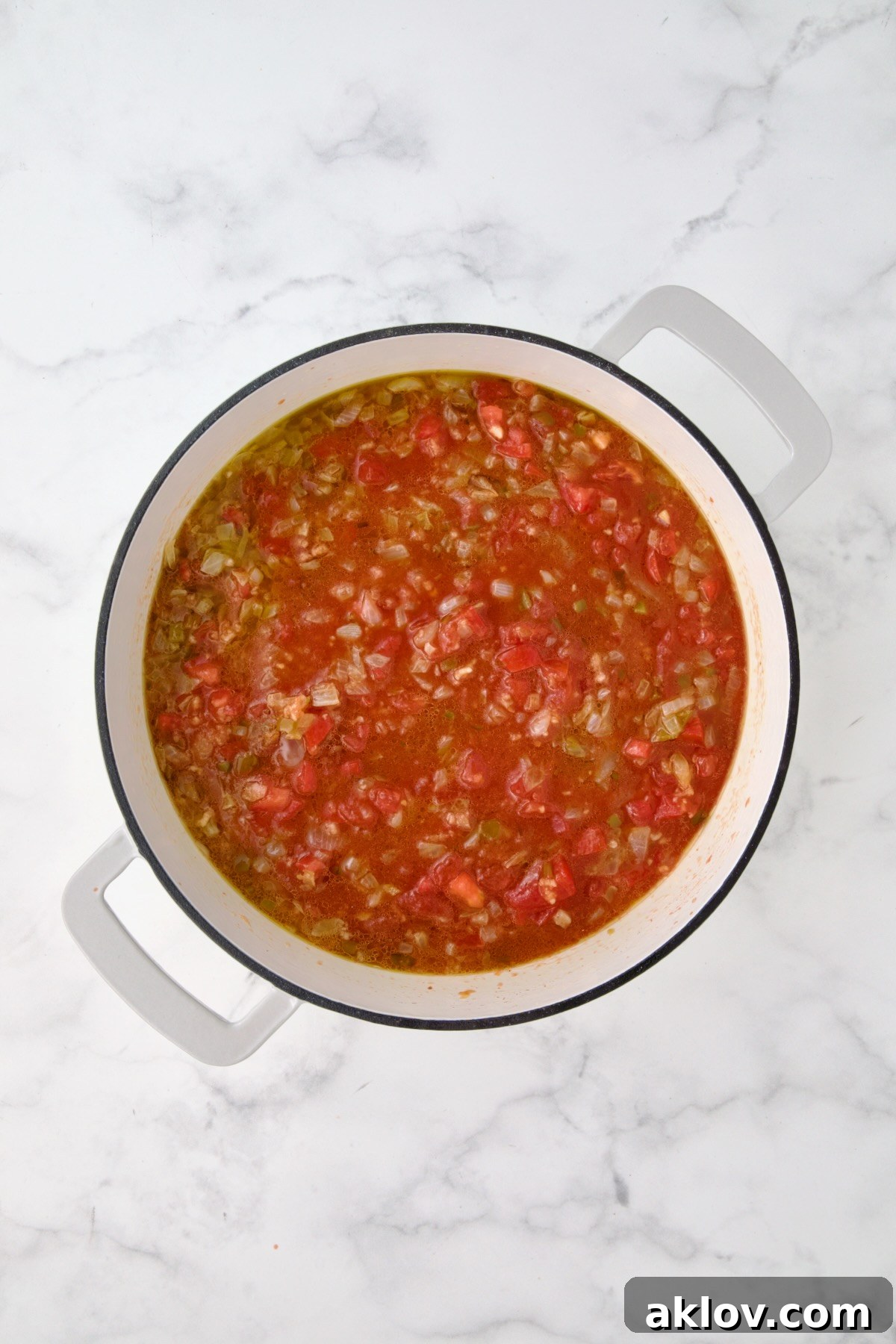 Tomatoes, diced tomatoes and water added to onions, peppers and garlic mixed together in white enamel cast iron skillet.