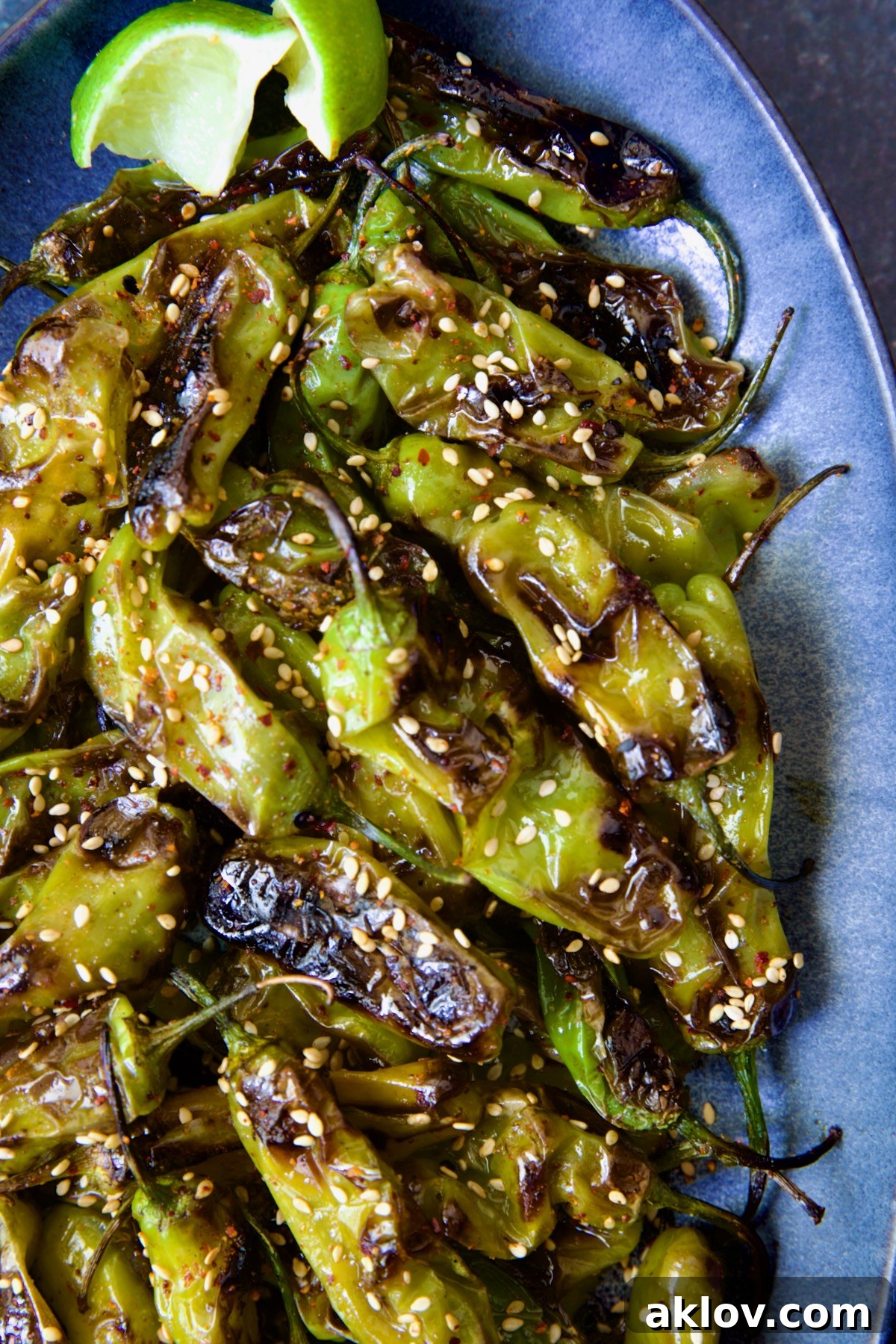 Blistered Shishito Peppers arranged beautifully on a blue oval platter, sprinkled with sesame seeds.