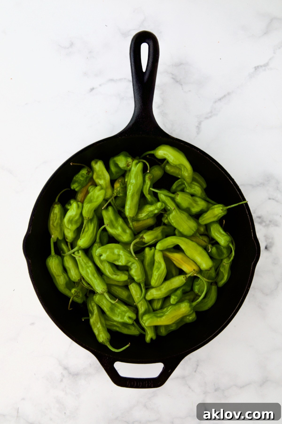 Shishito peppers neatly arranged in a black cast iron skillet, ready to be blistered.