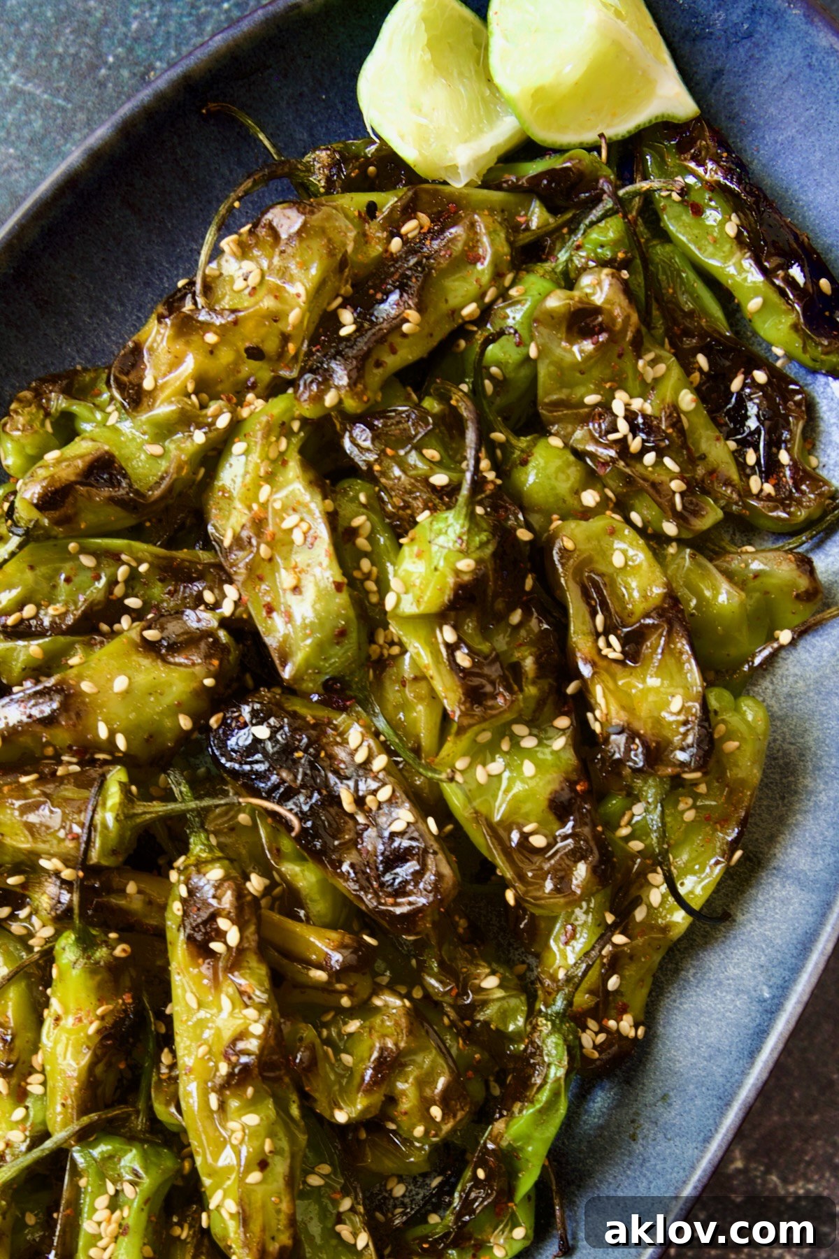 Blistered Shishito Peppers beautifully presented on a blue oval platter, garnished with sesame seeds.