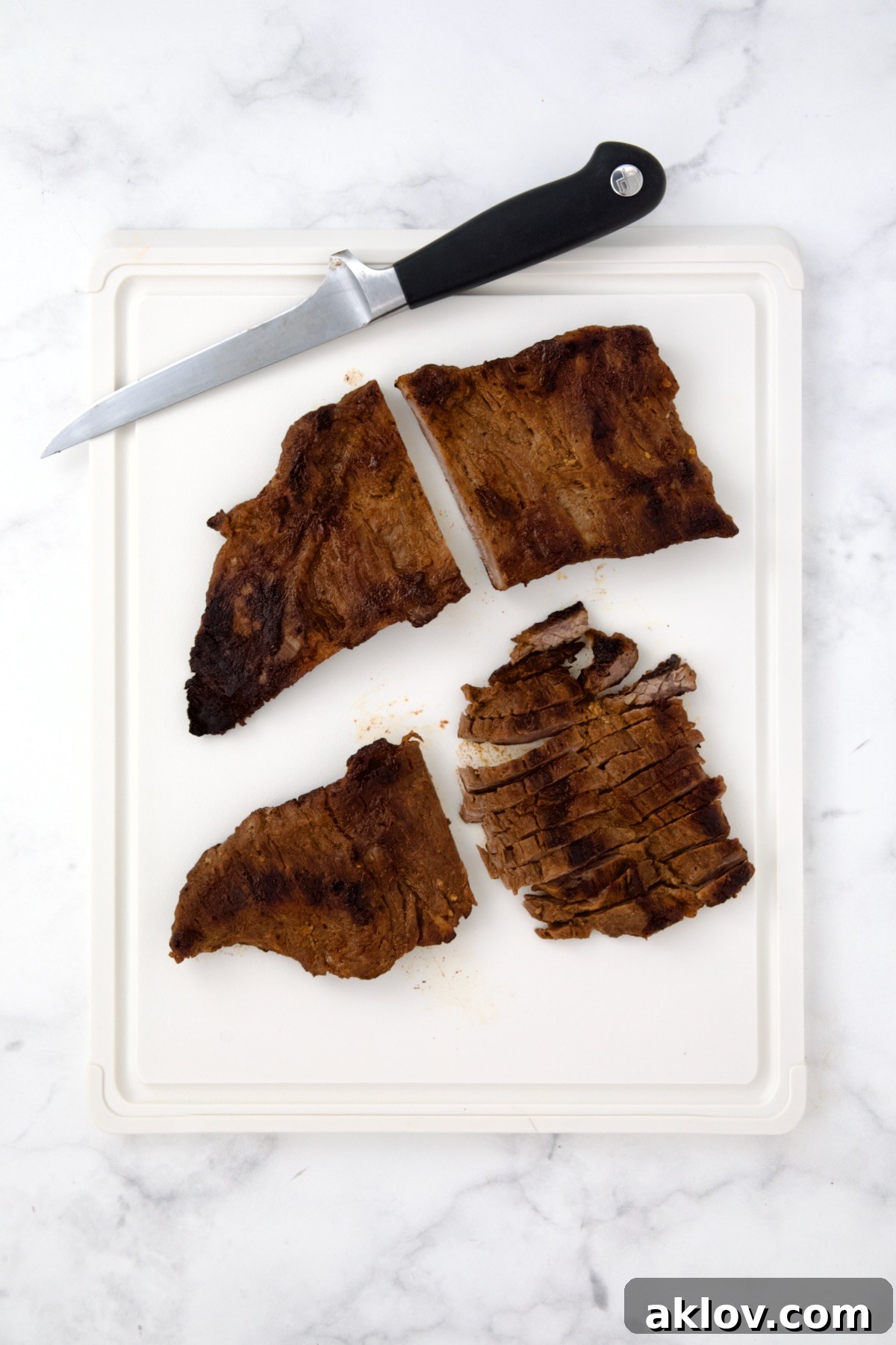 Two pieces of grilled skirt steak on white plastic cutting board being sliced.