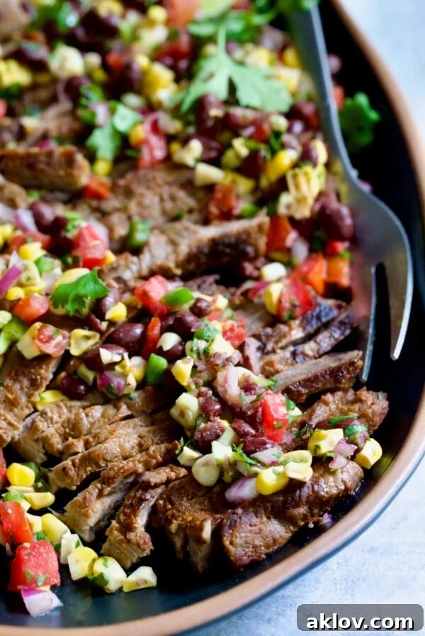 Grilled Skirt Steak with Black Bean Tomato Corn Salad on black platter with serving fork.