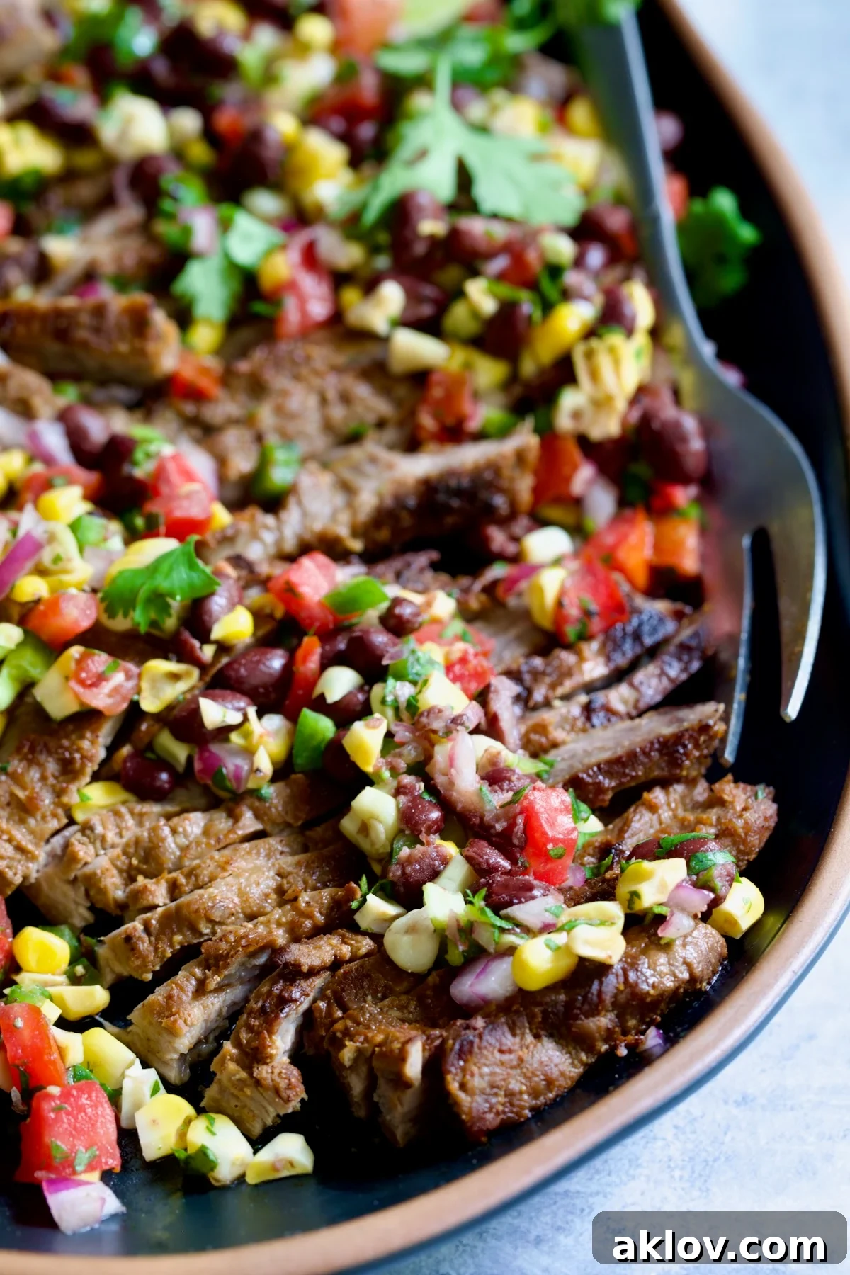 Grilled Skirt Steak with Black Bean Tomato Corn Salad on black platter with serving fork.