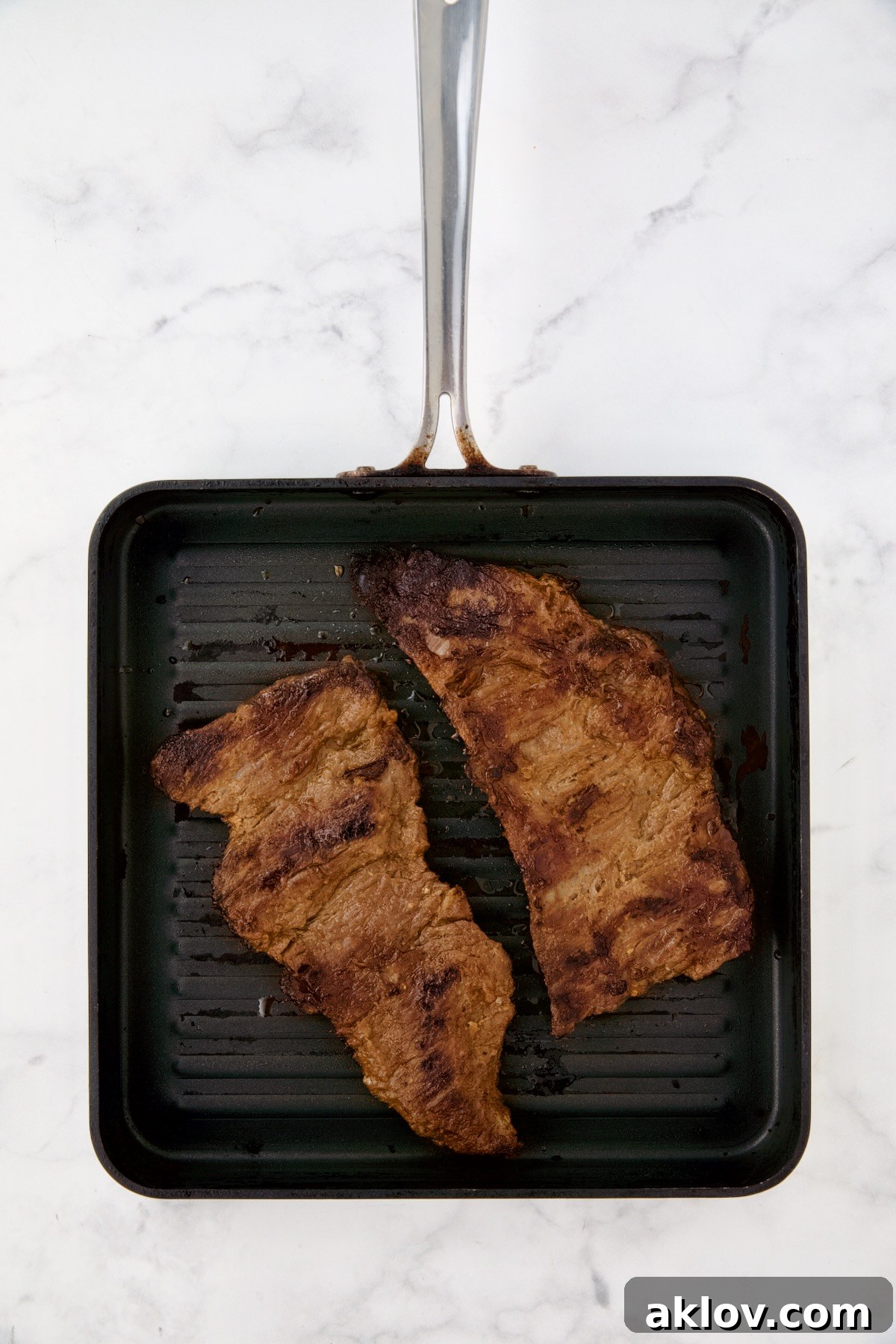 Two pieces of grilled skirt steak on grill pan.
