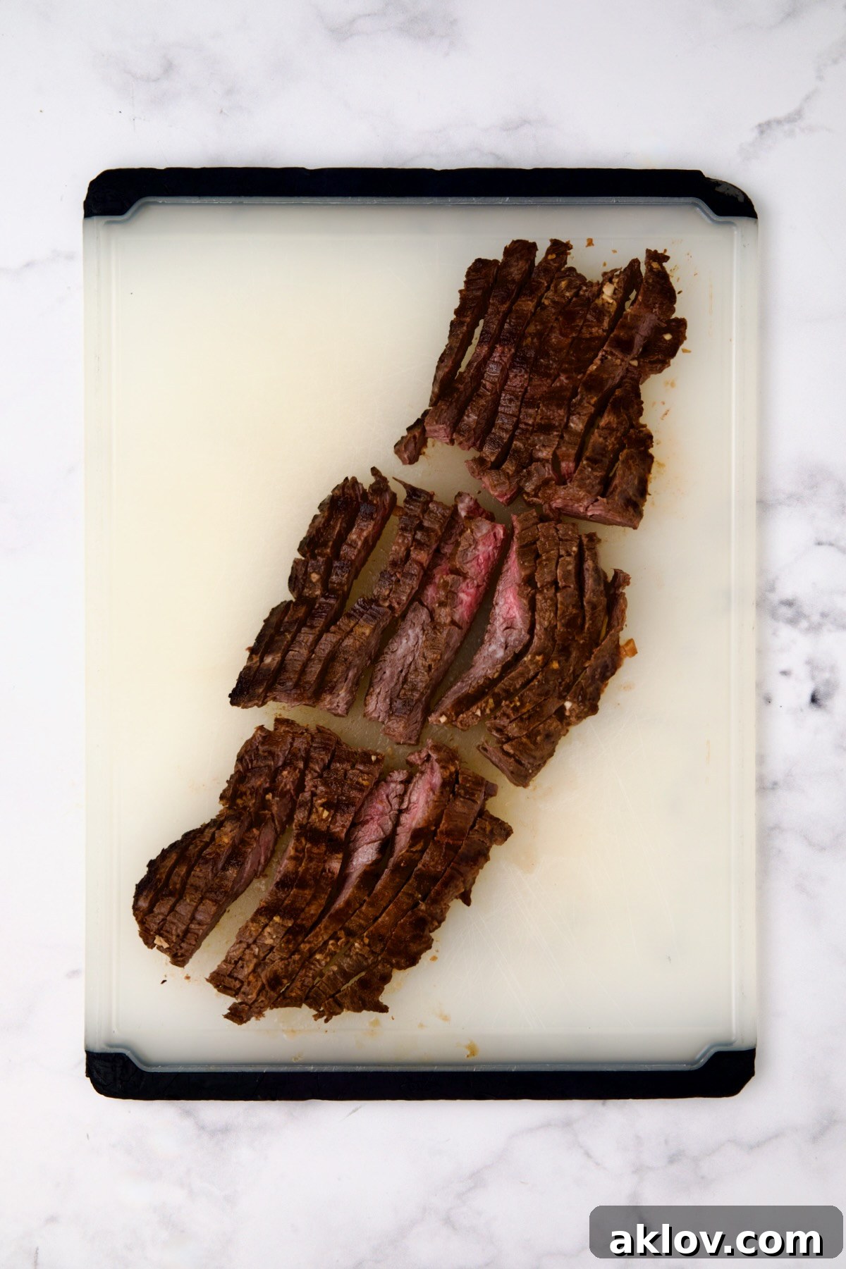 Grilled skirt steak on a white plastic cutting board after being sliced.
