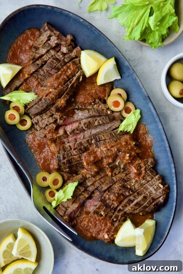 Sliced Bloody Mary Skirt Steak on blue oval platter garnished with lemon wedges, olive slices and celery leaves.