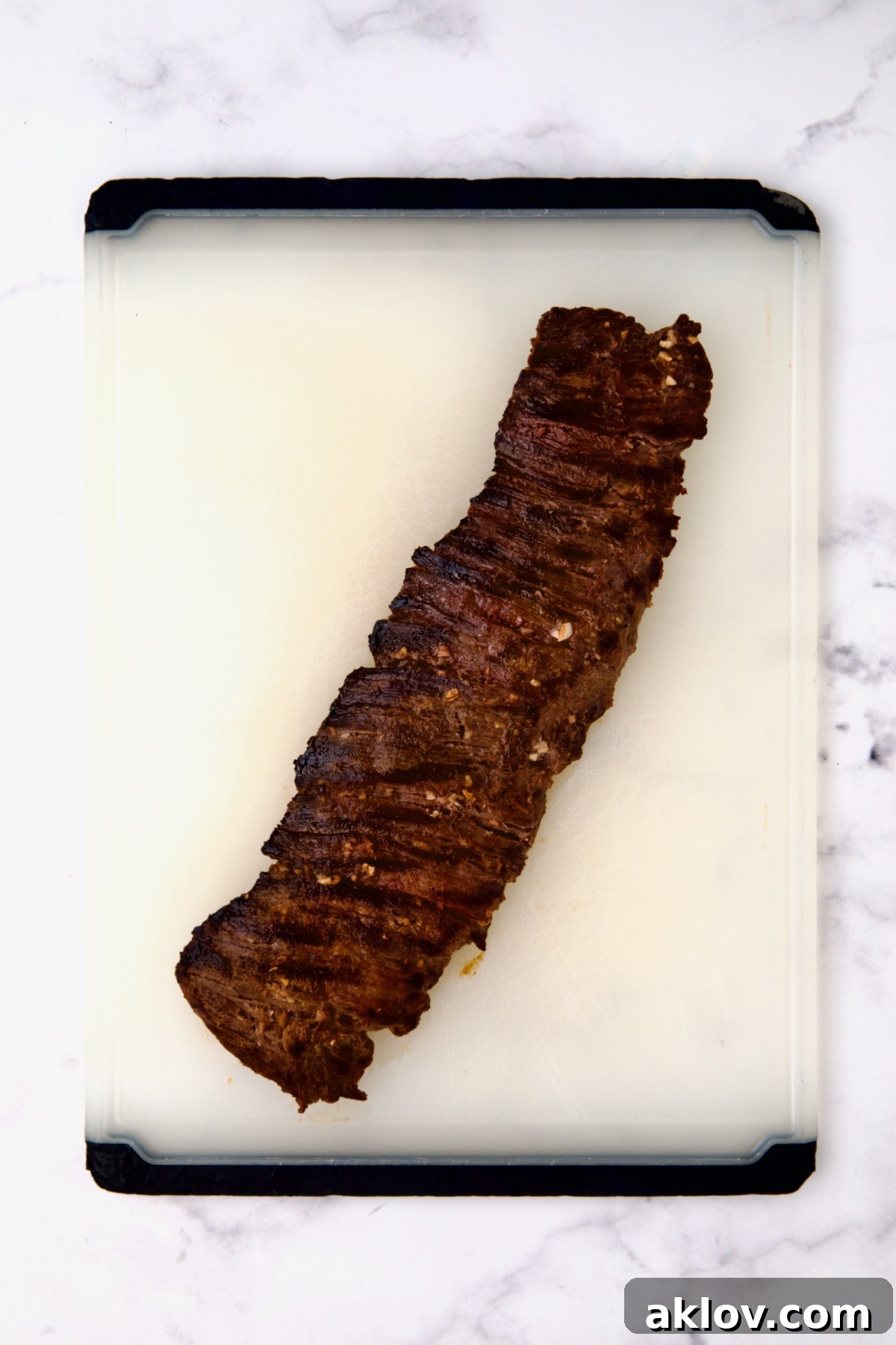 Grilled skirt steak on white plastic cutting board before being sliced.