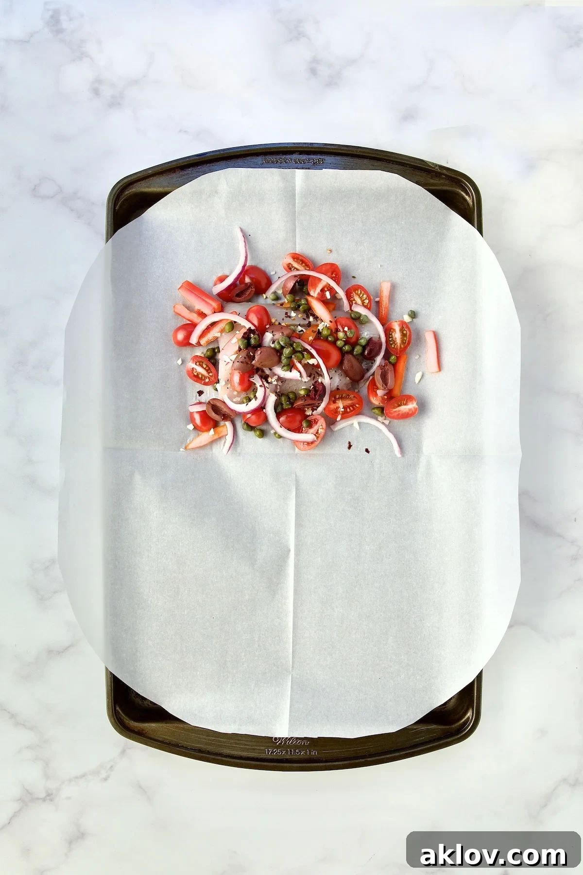 Flavorful Mediterranean Fish Parcels 9 Uncooked fish with other ingredients on parchment paper on rimmed sheet pan.