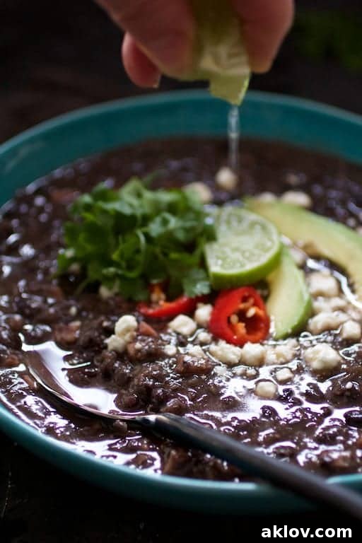 A hand squeezing fresh lime juice over a bowl of Slow Cooker Black Bean Soup with Ham, beautifully garnished, emphasizing the final touch of freshness.