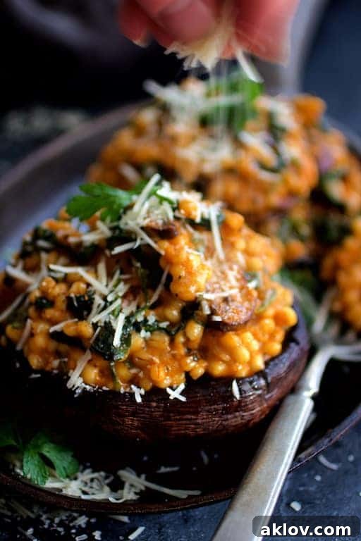 Photo of Barley Risotto Stuffed Portobello Mushrooms being sprinkled with Parmesan cheese for a finishing touch.