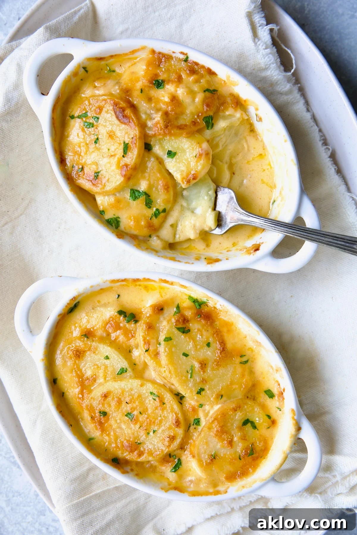 Two white oval dishes of perfectly baked Au Gratin Potatoes for Two, with a fork digging into one, showing the creamy layers.