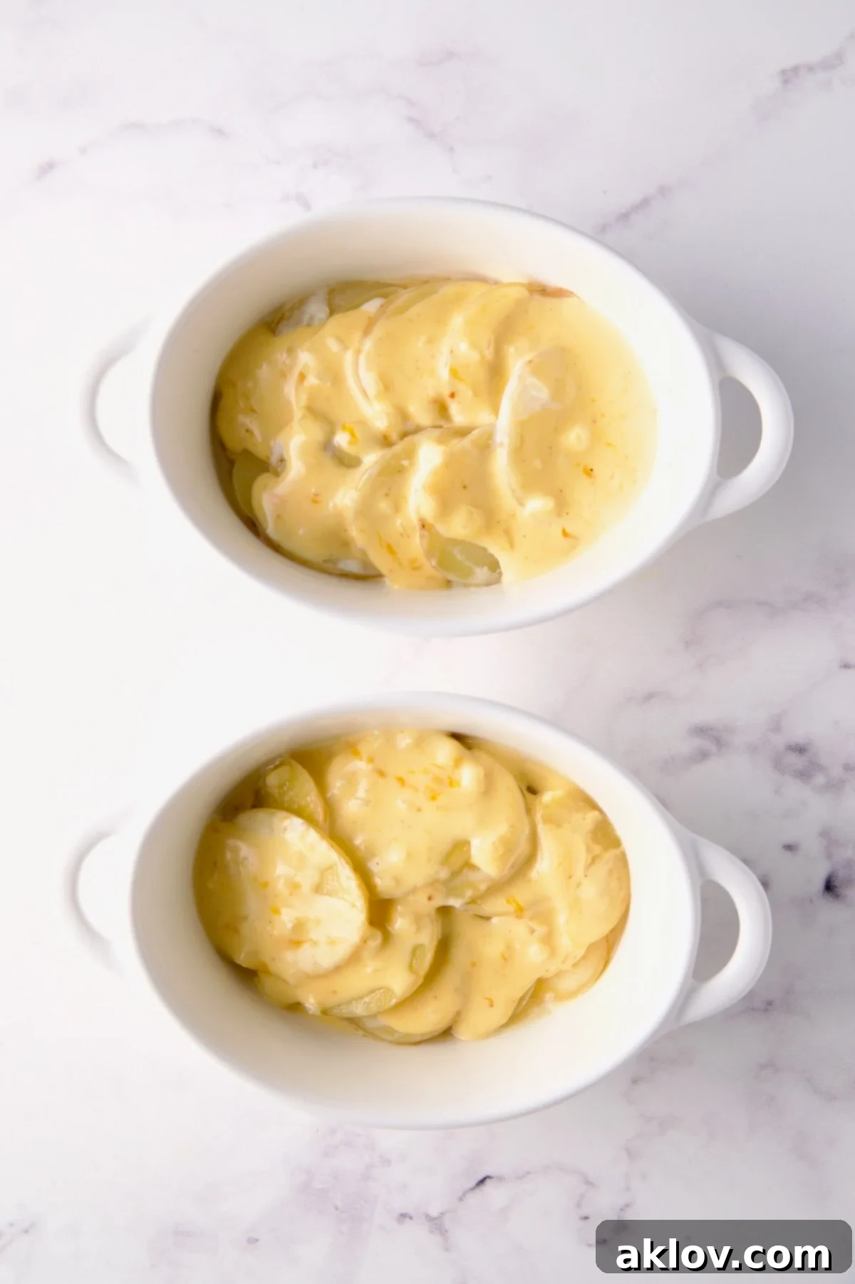 Two oval dishes, each with the first layer of potatoes and a drizzle of cheese sauce, ready for more layers.