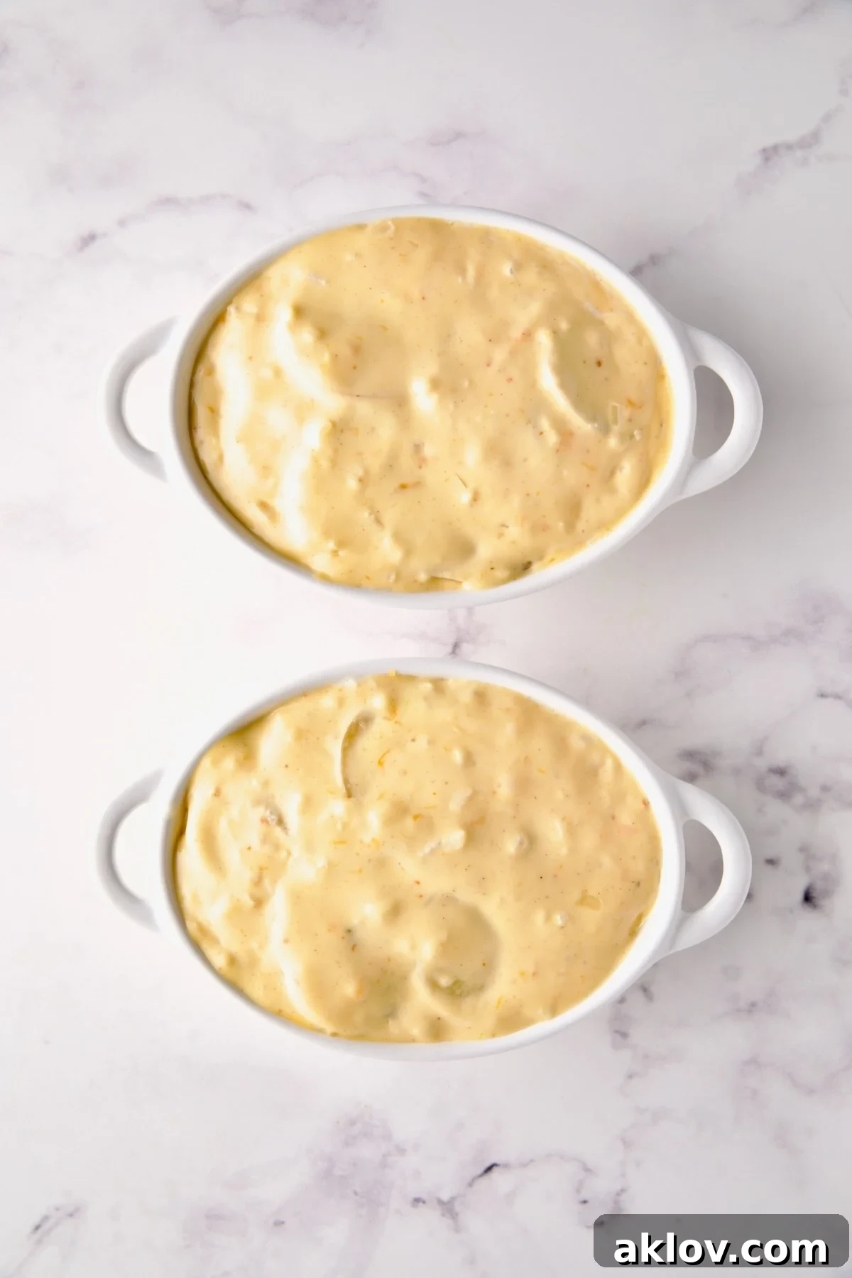 Fully assembled au gratin potatoes in white oval dishes, generously covered in cheese sauce, poised for baking.