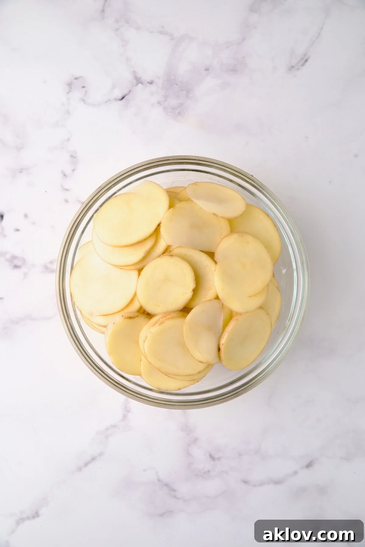 Thinly sliced Yukon Gold potatoes neatly arranged in a clear glass bowl, showcasing their uniform cuts.