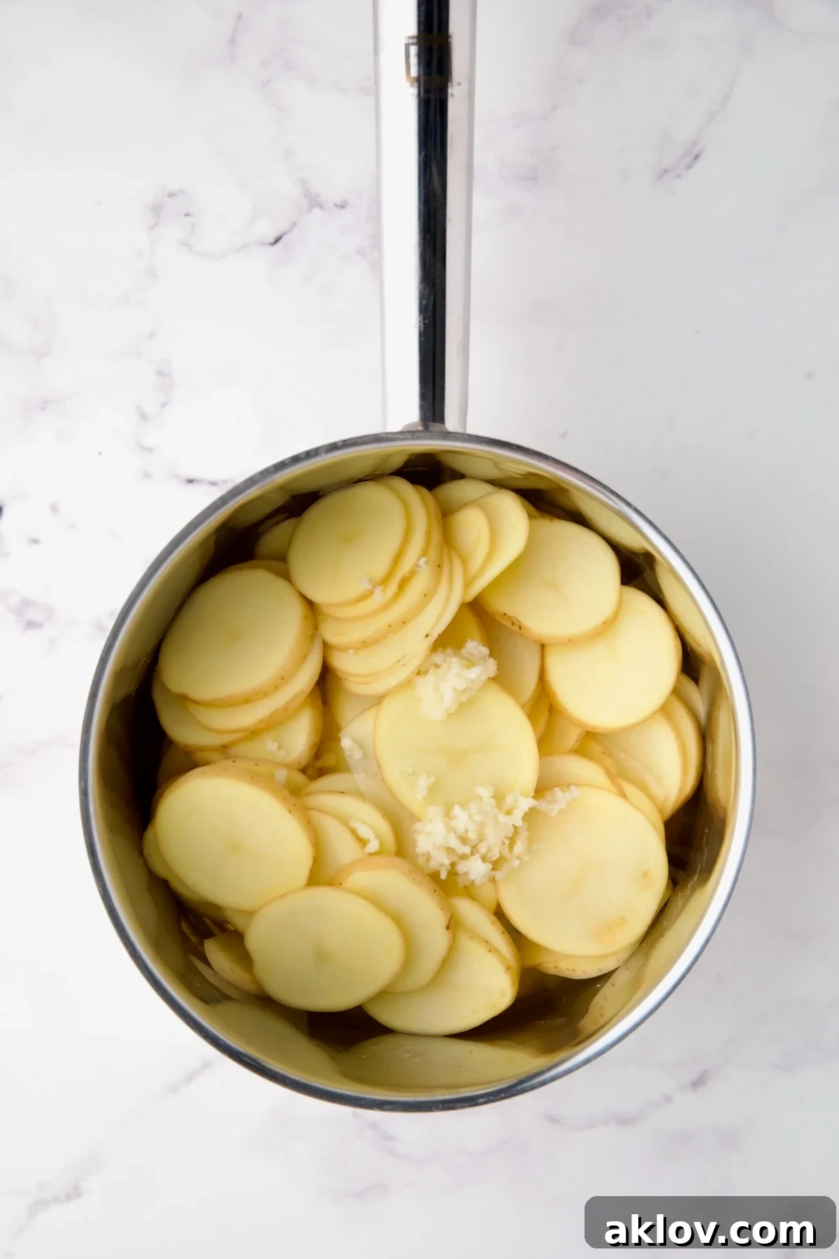 Thinly sliced Yukon Gold potatoes, onion, and garlic nestled in a stainless steel saucepan, ready for cooking.